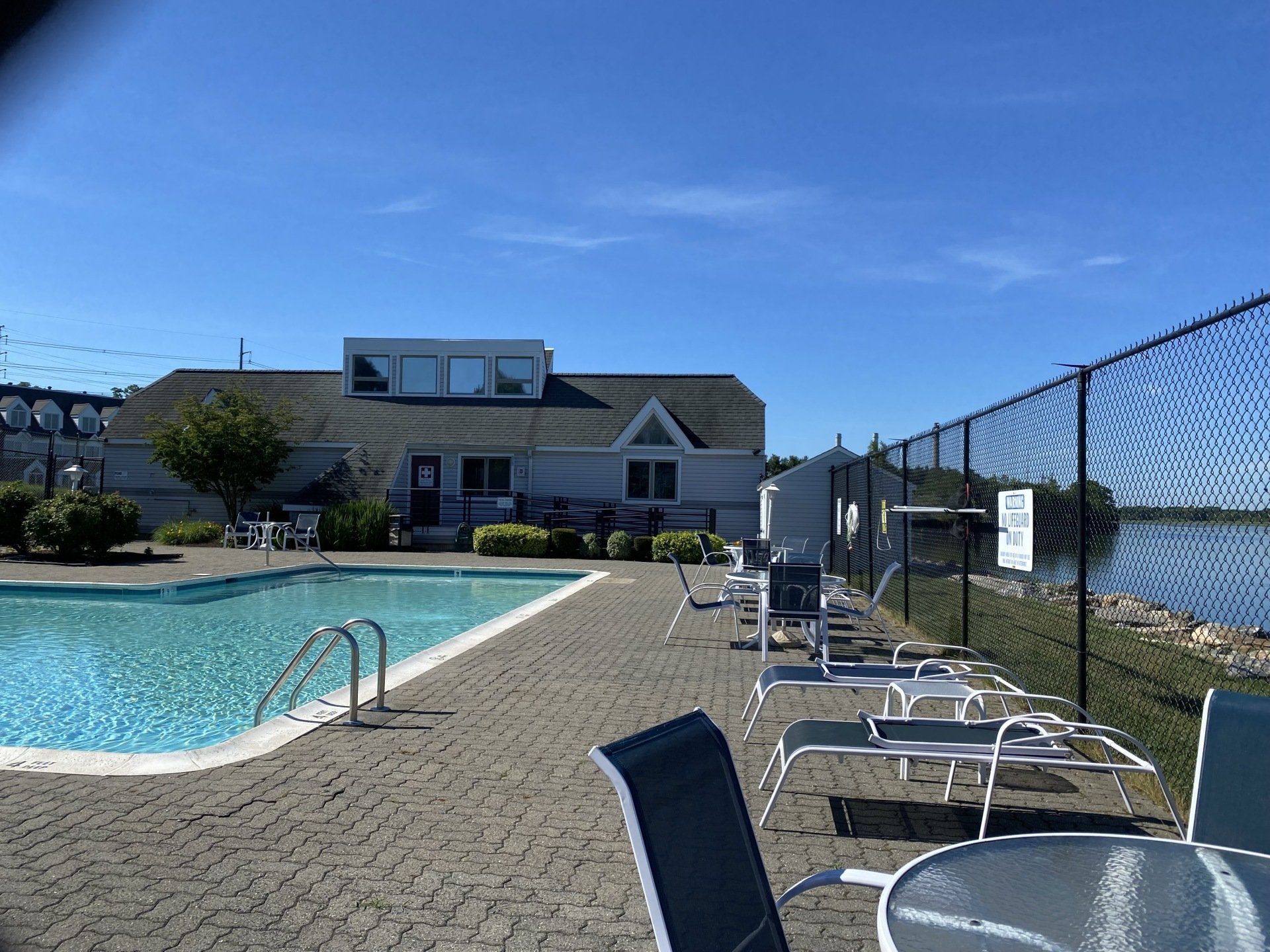 Poolside scene: pool, lounge chairs, building with windows, water, blue sky.