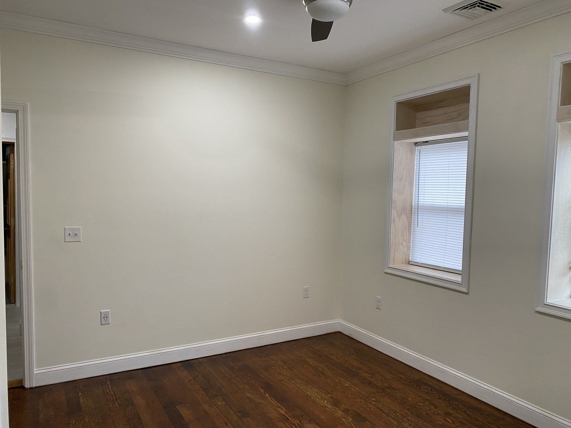 Empty room with wooden floor, white walls, two windows, and crown molding.