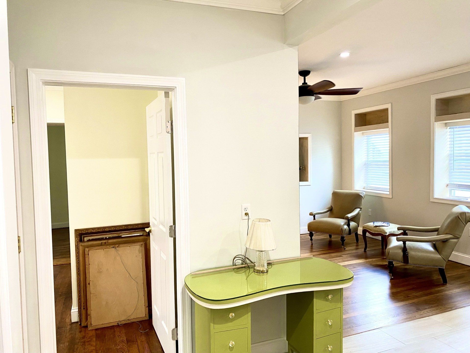 Interior with desk, open door, and living area with chairs. Green desk, light walls, and hardwood floors.