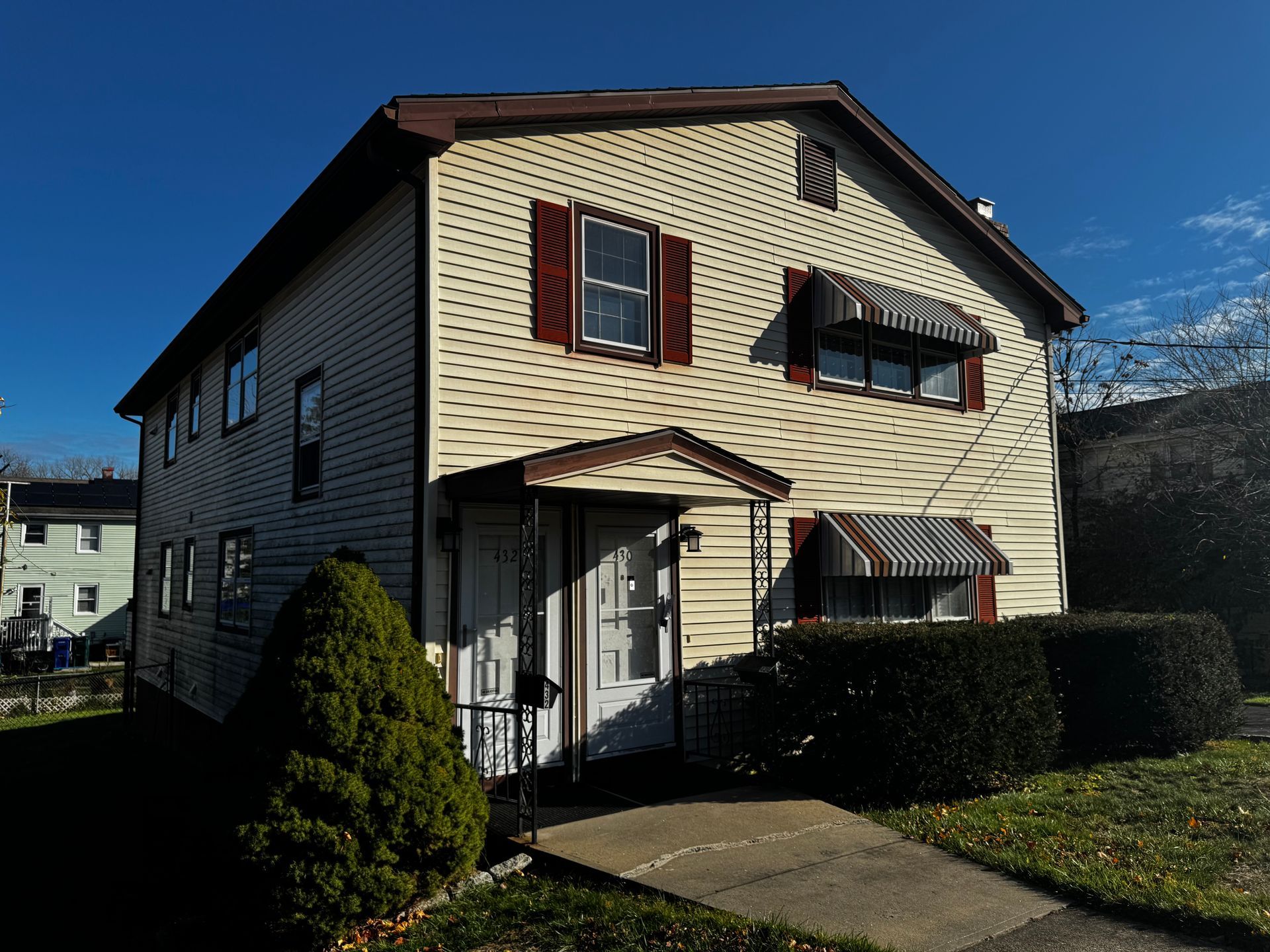 Red house behind a stone wall, trees surround, blue sky.