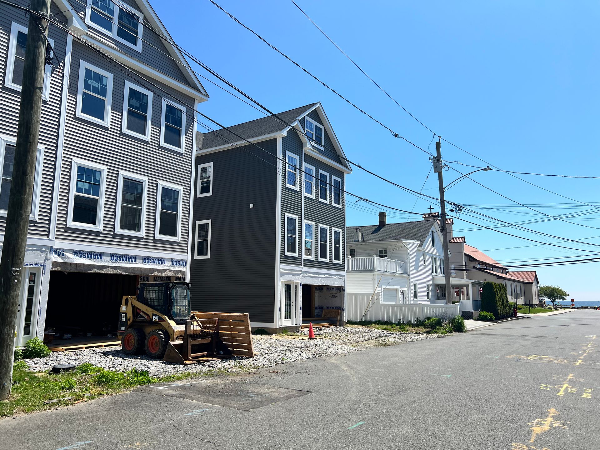 Row of multi-story houses under construction, gray and blue siding, on a sunny day.