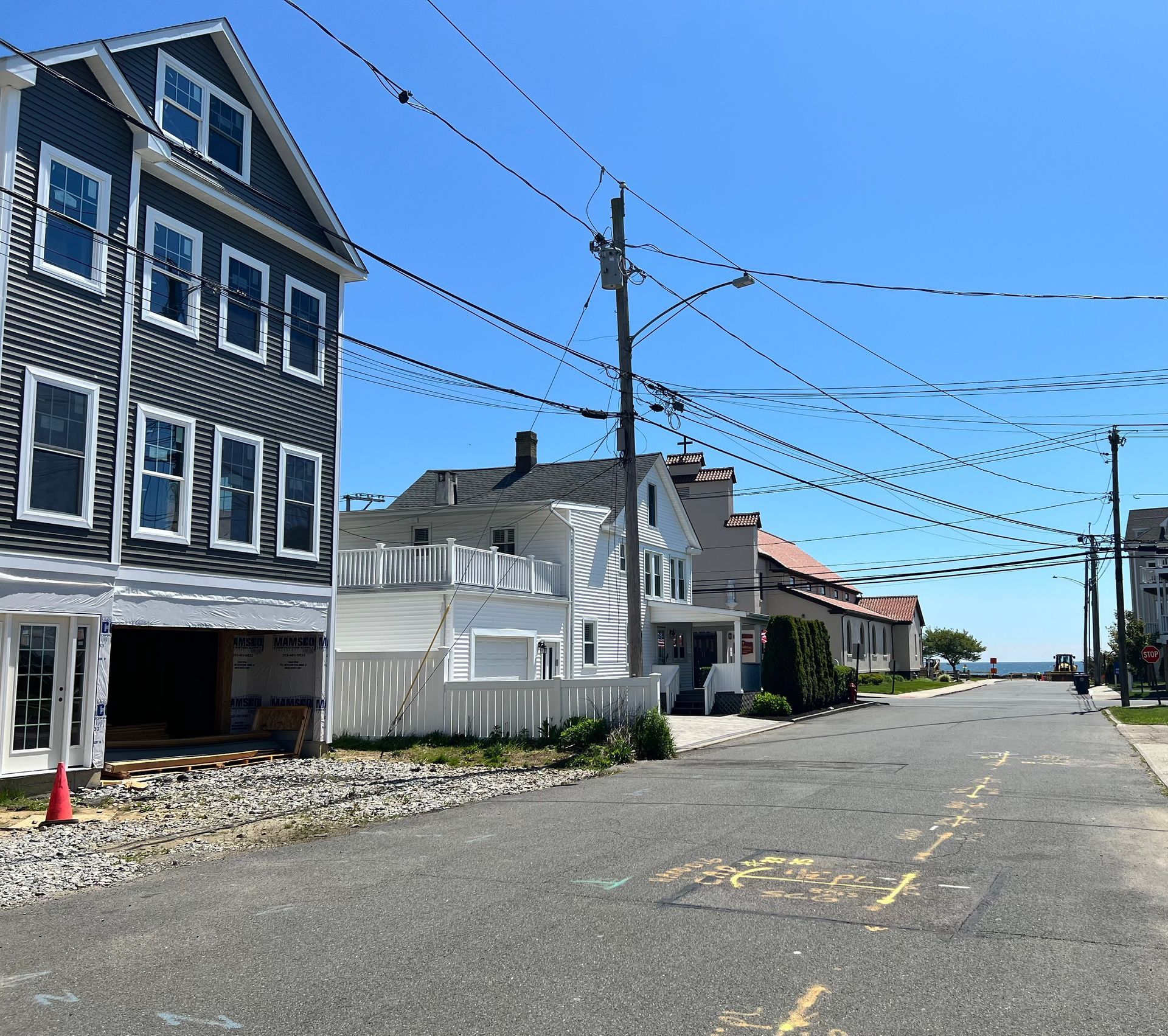 Street with houses, power lines, and blue sky. Buildings have various colors and styles; some are under construction.