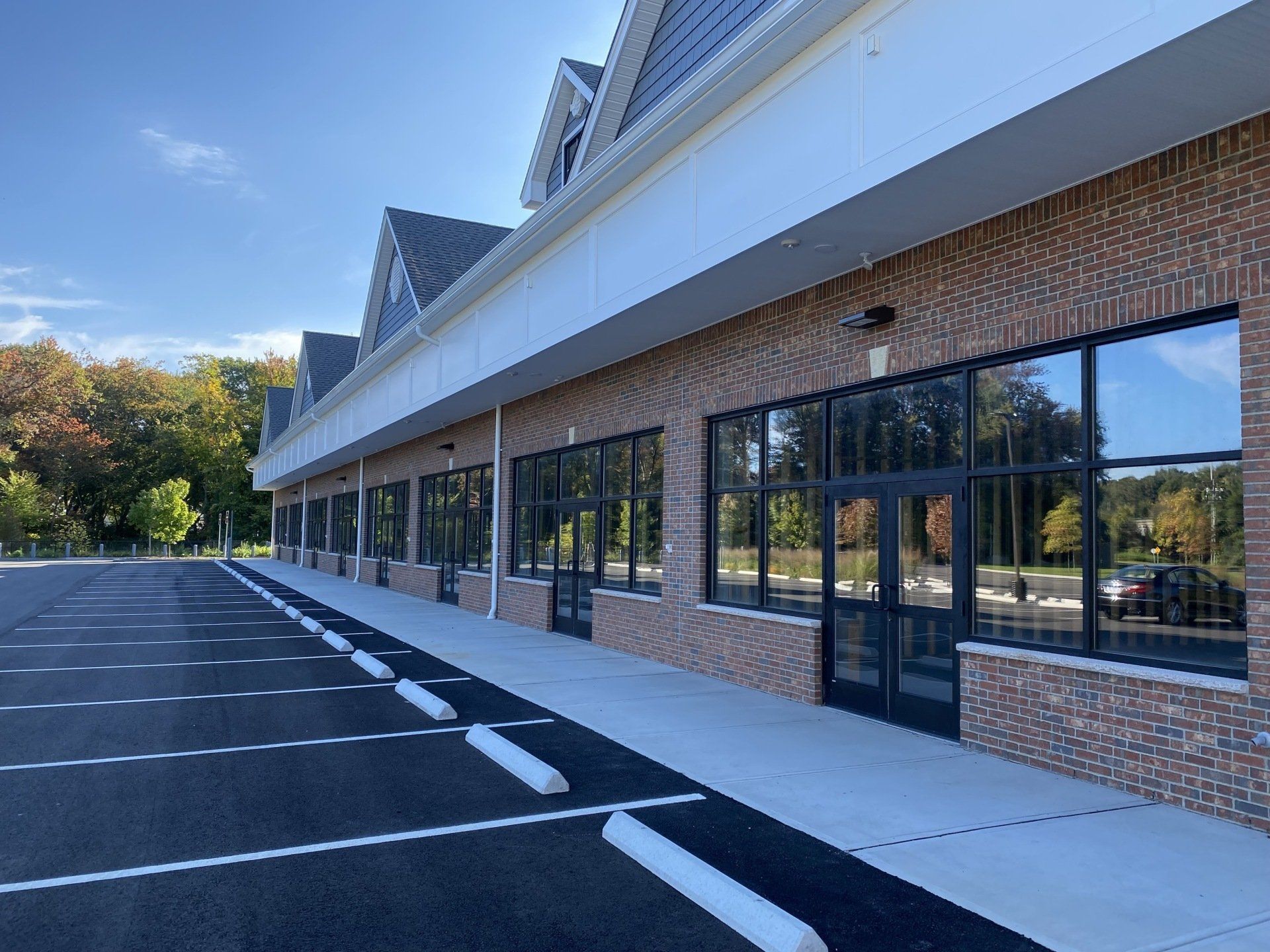 Exterior view of a brick commercial building with large windows and a parking lot on a sunny day.