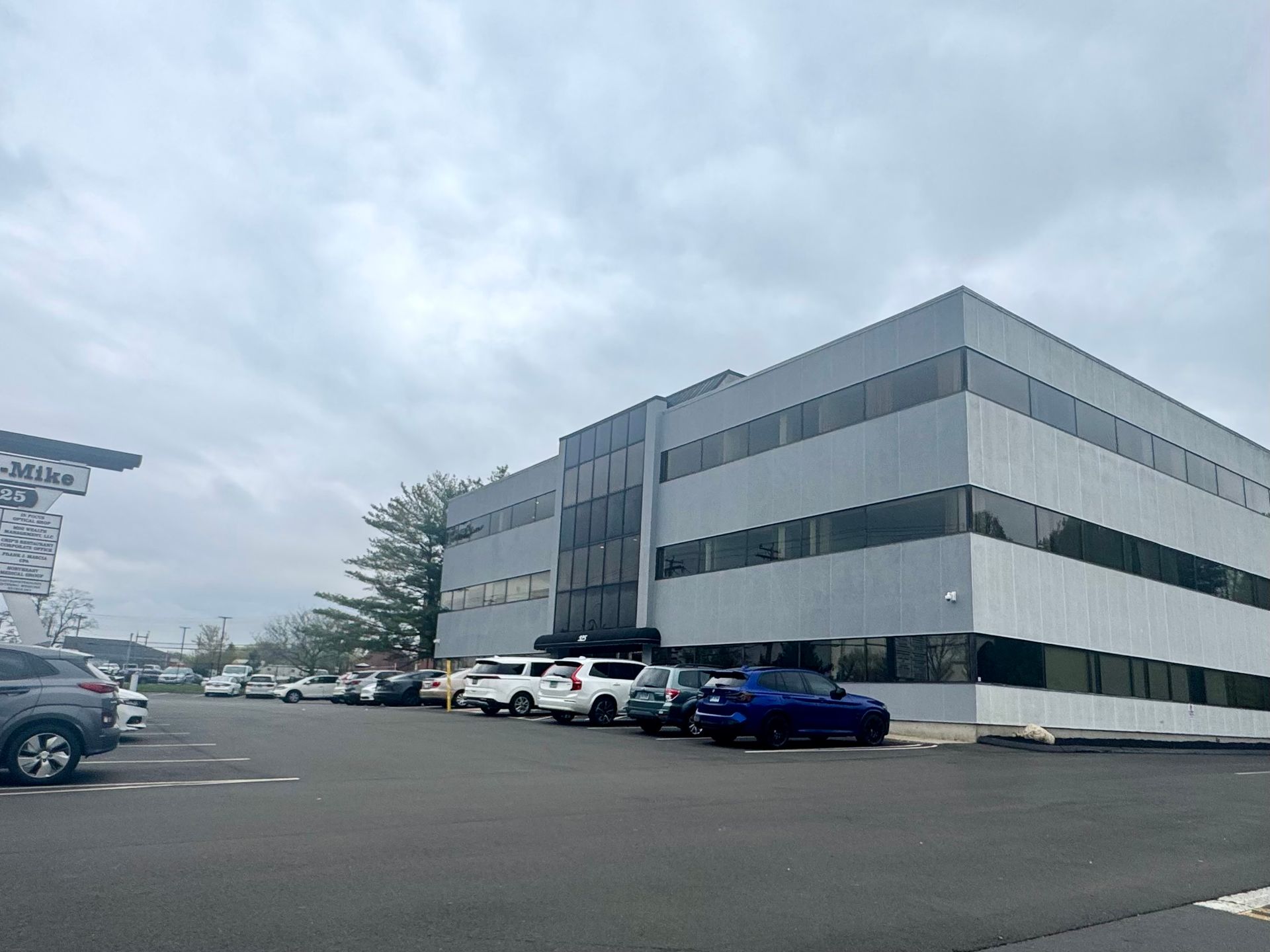 Office building with black and white facade; cars parked in front on a sunny day.