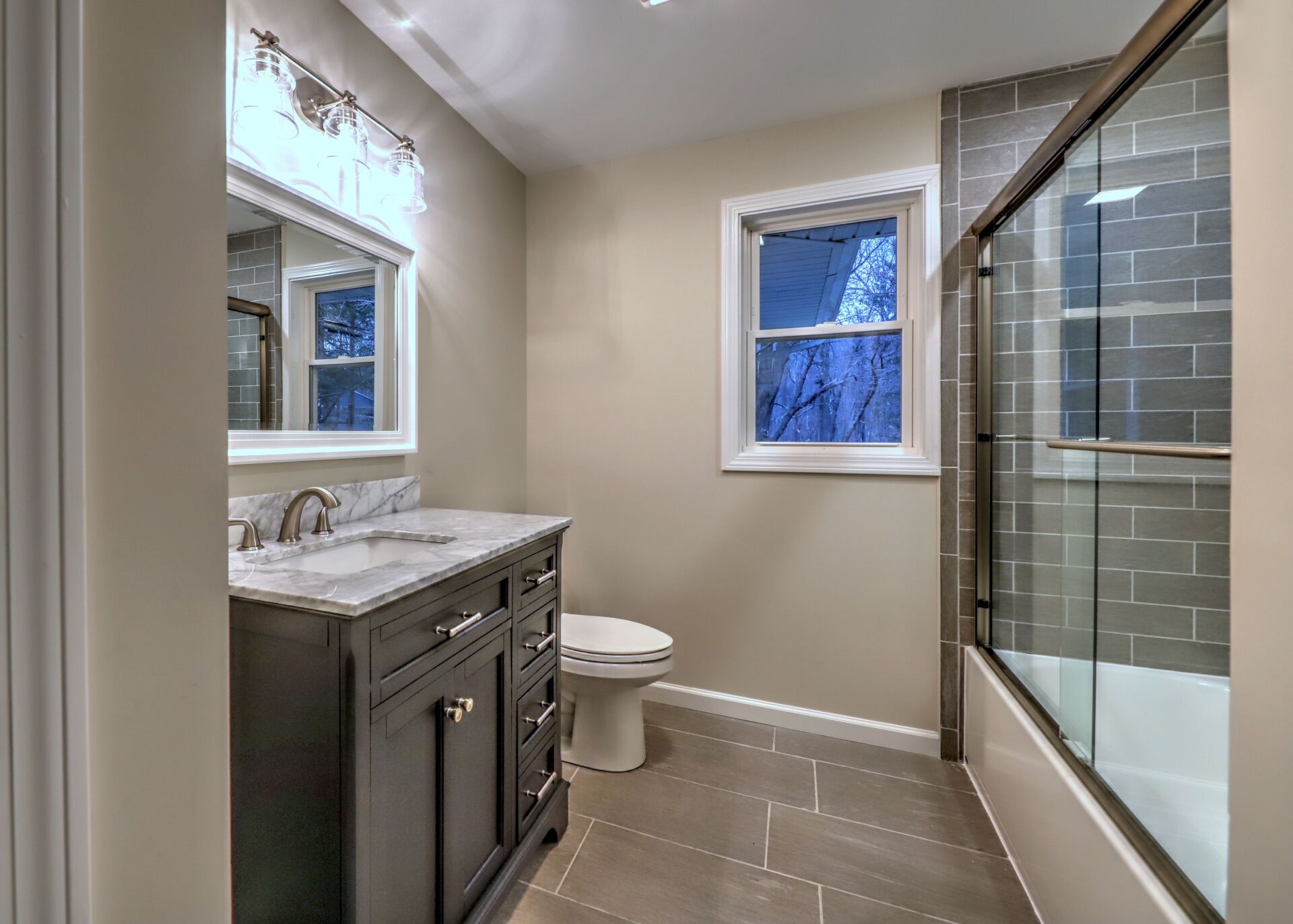 Bathroom with a dark gray vanity, gray tiled floor, and a glass shower door.