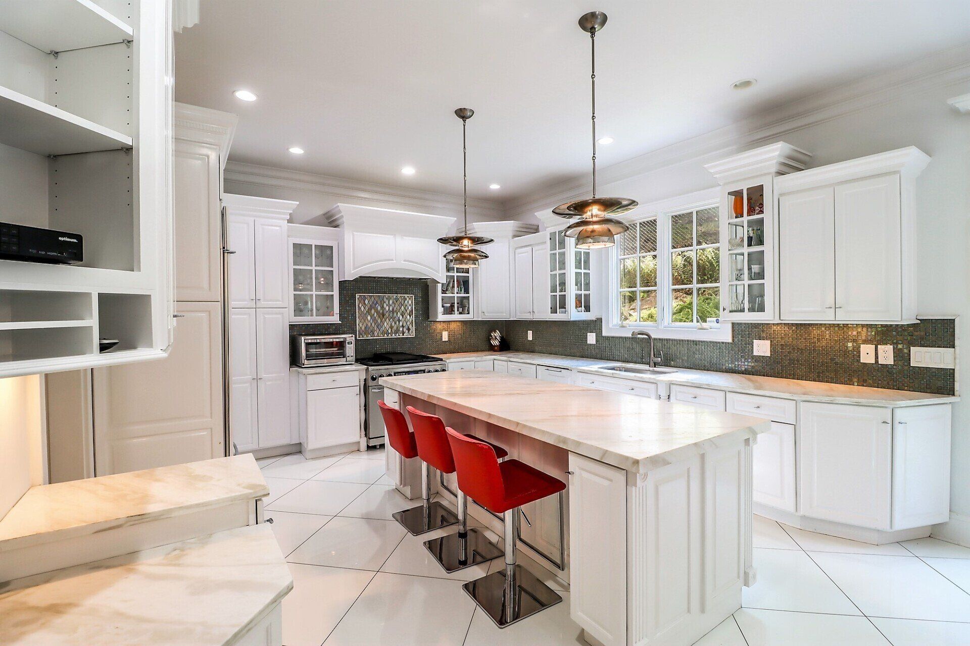 White kitchen with island, red bar stools, and pendant lights.