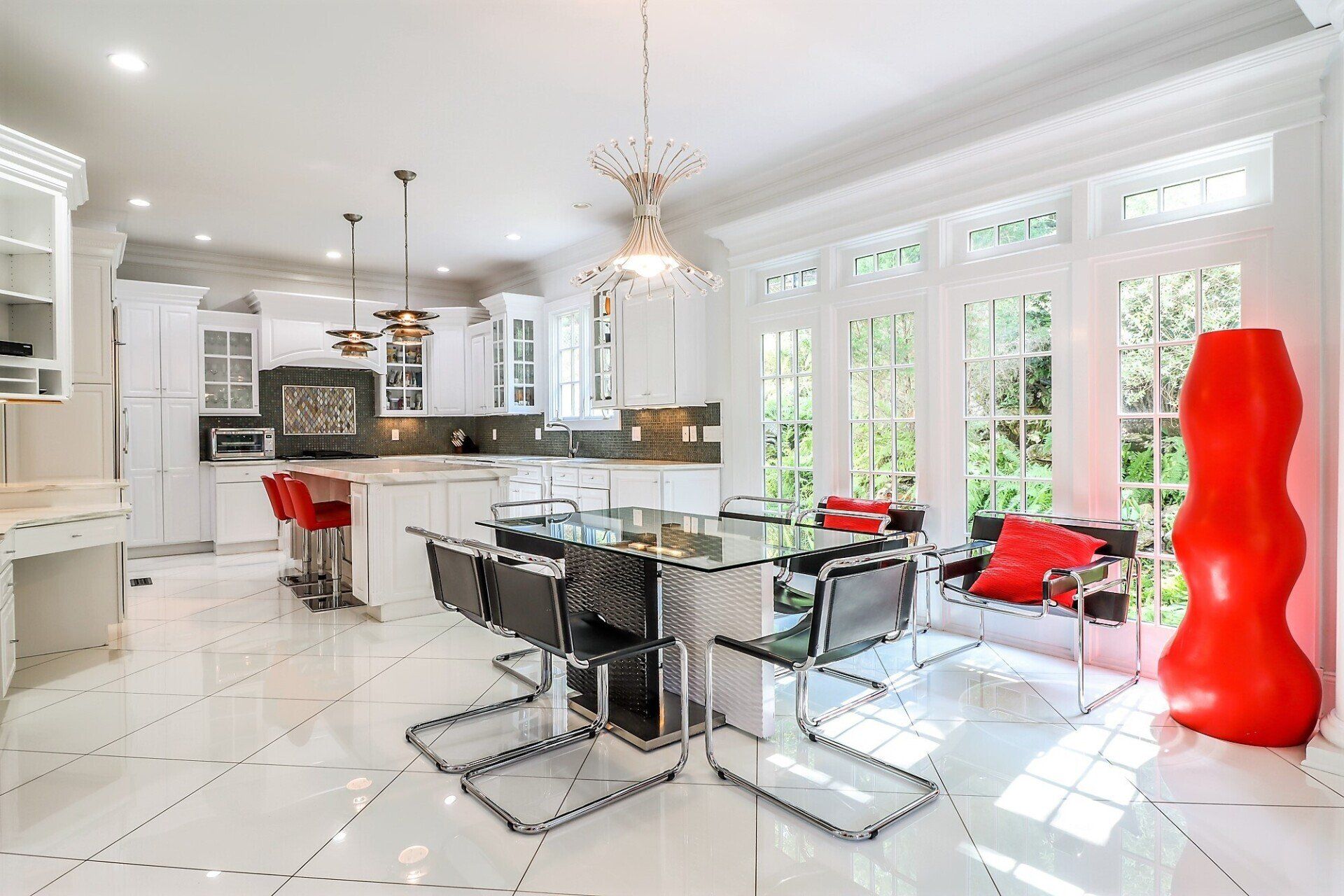 Bright white kitchen and dining room with modern furniture, red accents, and a large red sculpture.