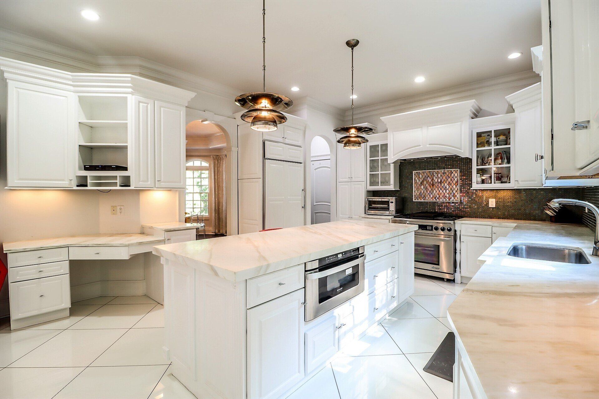 White kitchen with marble countertops, stainless steel appliances, and pendant lights.