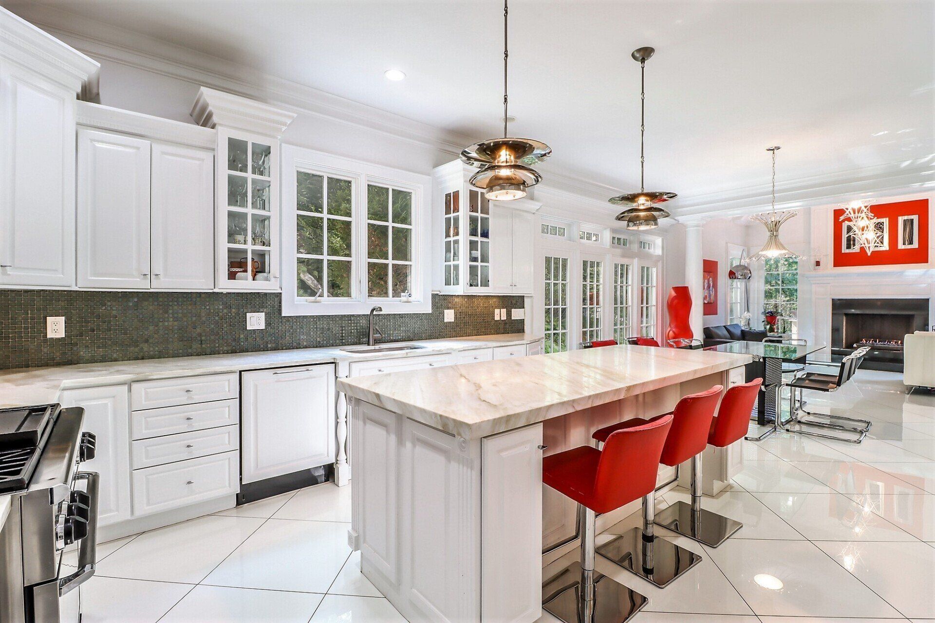 White kitchen with marble countertops, island with red stools, and open to a living room.