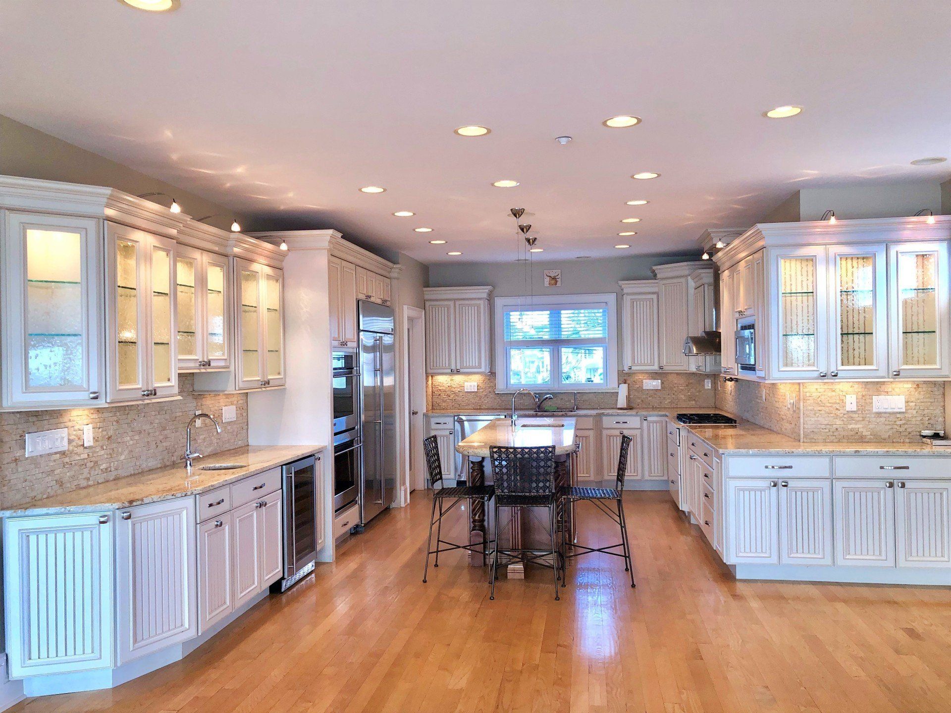 Spacious kitchen with white cabinets, granite countertops, stainless steel appliances, and wood floors.