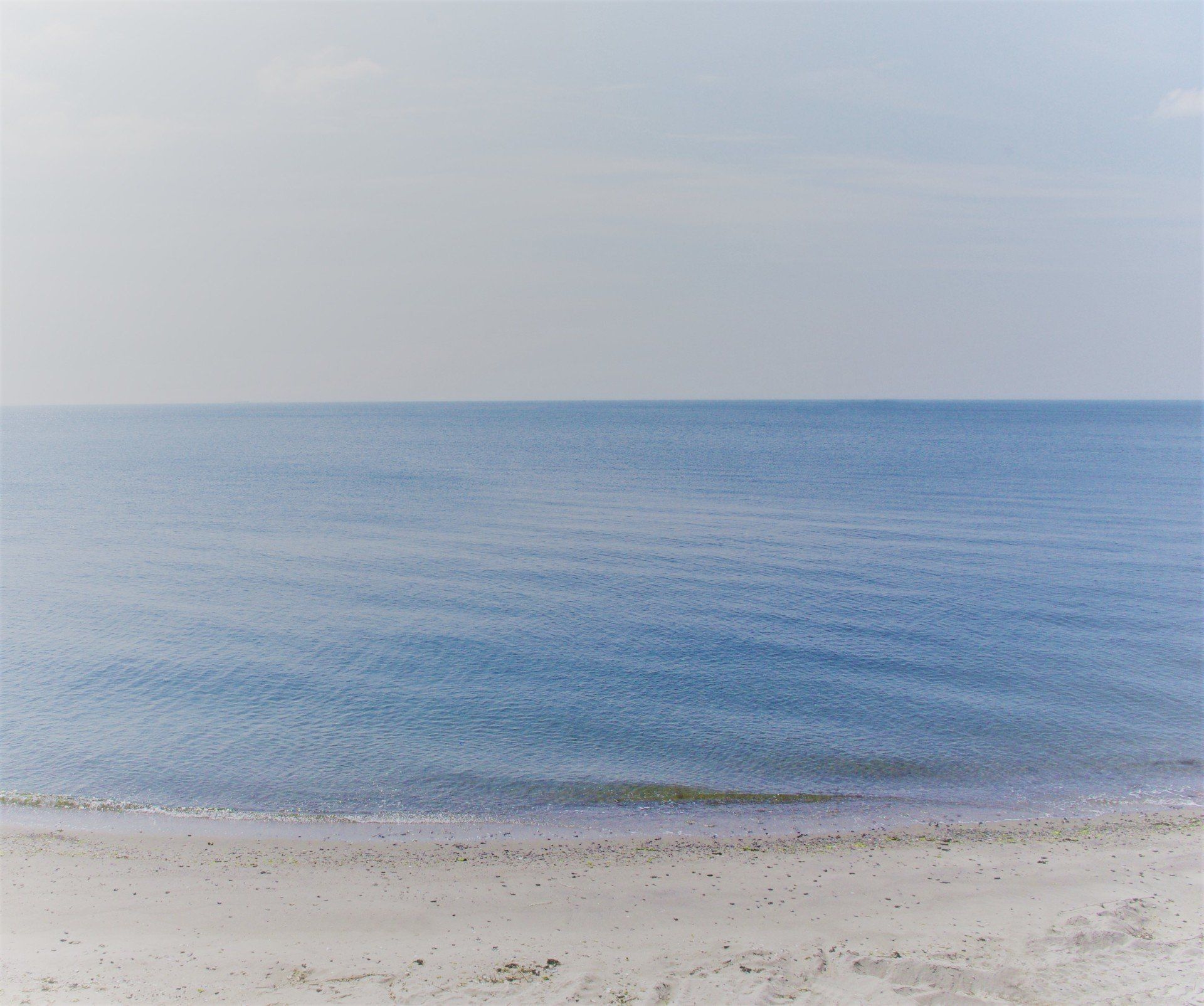 Blue ocean meets a light sandy beach under a hazy sky.