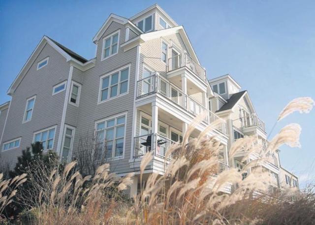 Multi-story beige building with white trim, balconies, and dormers, viewed from below through tall, dried grasses.