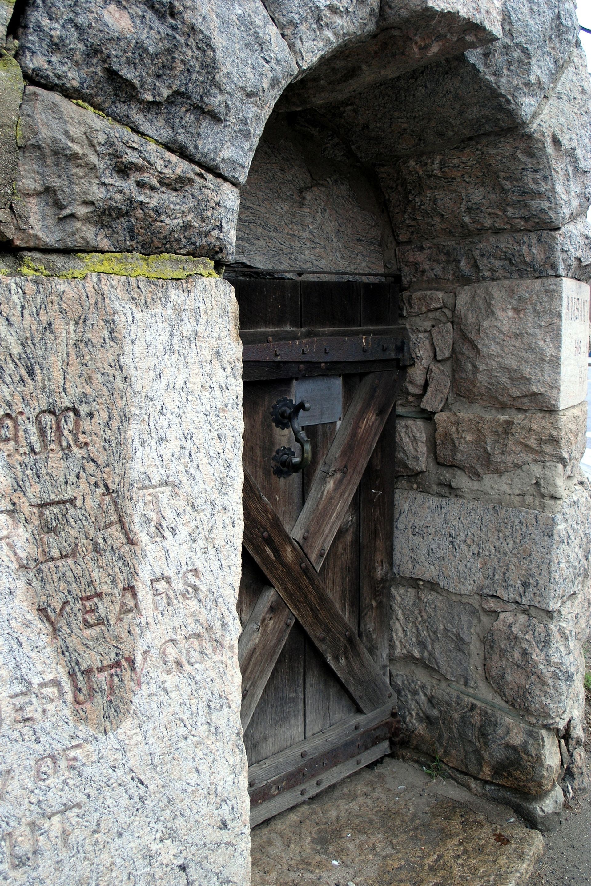 Stone archway with wooden X-braced door. Etched inscriptions on the left stone wall.