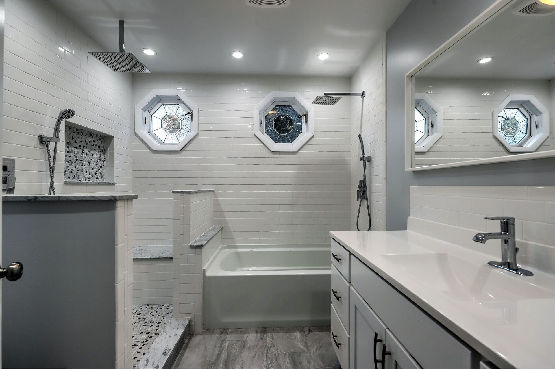 Modern bathroom with white and gray tile, octagonal windows, a shower, and vanity.