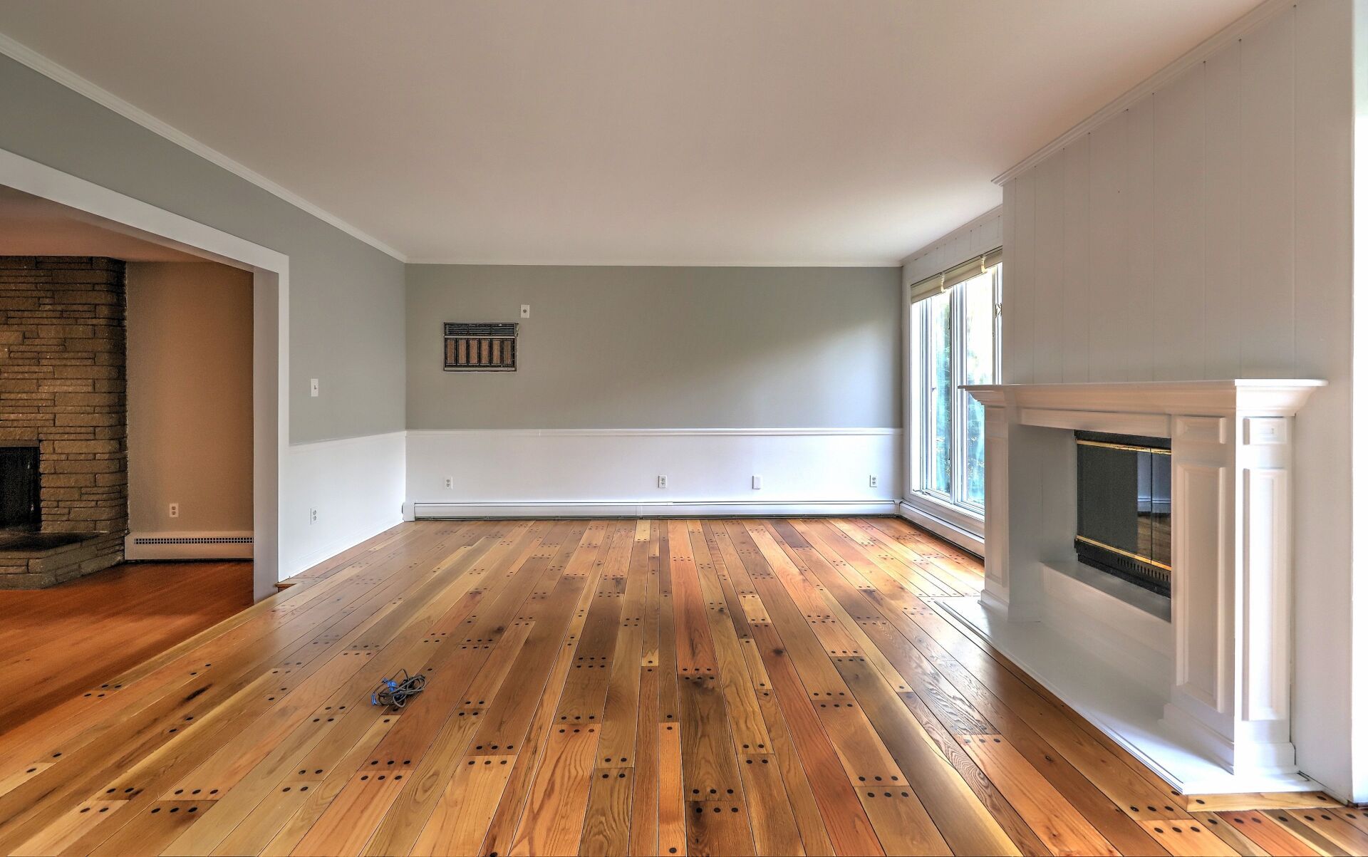 Empty living room with wood floors, fireplace, and large windows. Walls are gray and white.