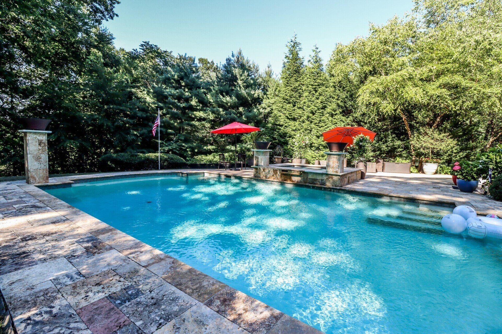 Swimming pool with red umbrellas, stone deck, and lush trees.
