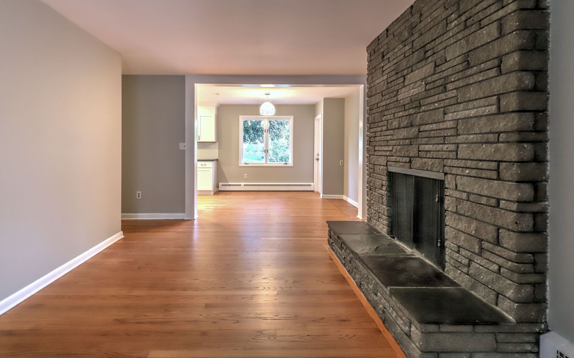 Living room with stone fireplace, wood floor, and doorway to another room.