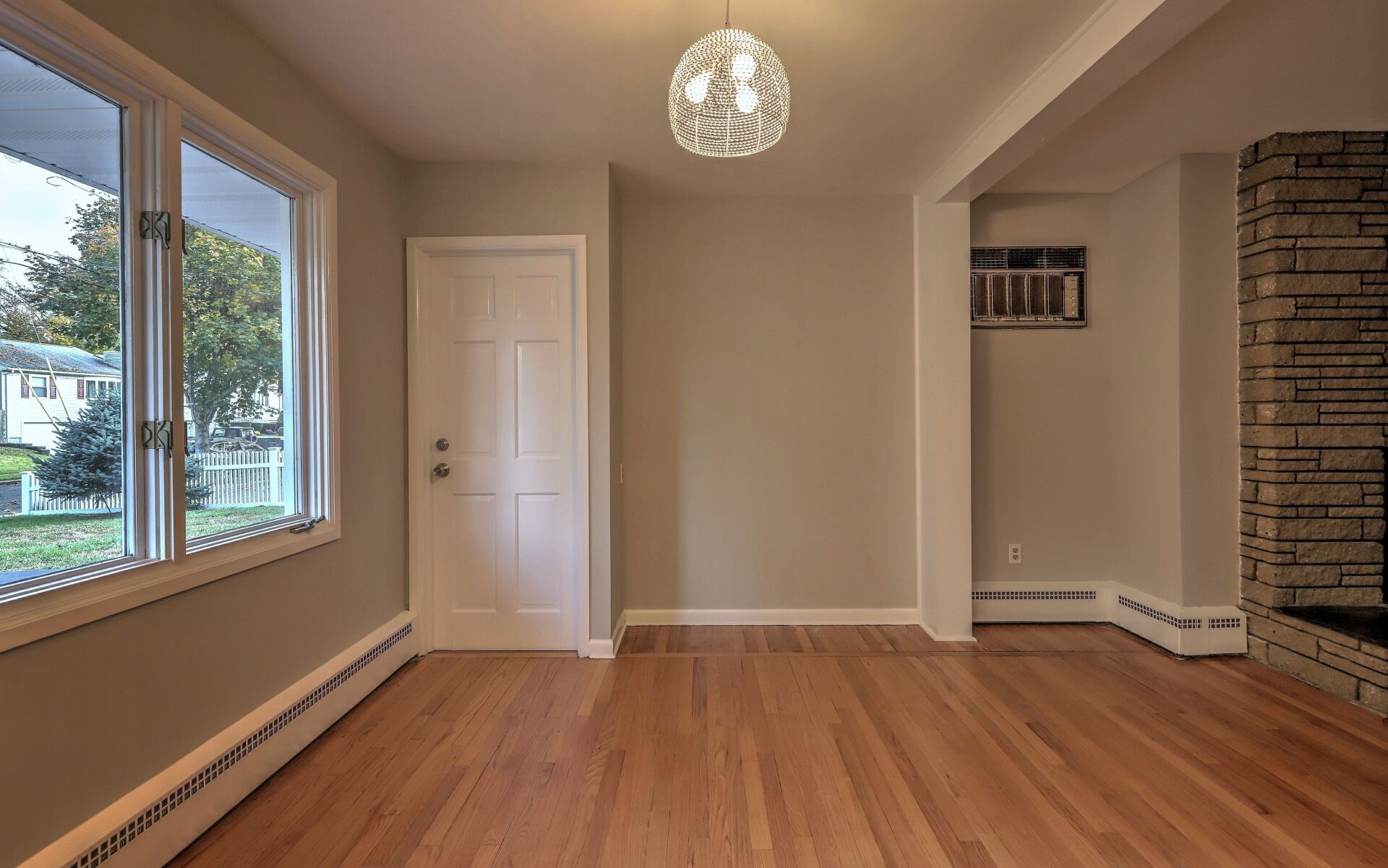 Empty room with hardwood floors, a door, windows, and a stone fireplace.