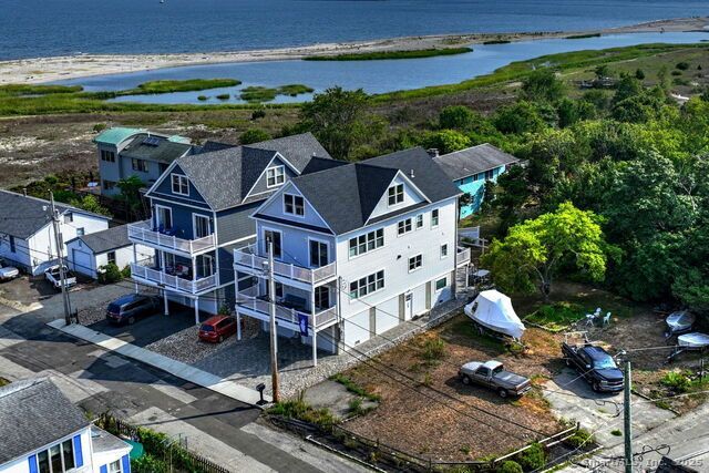 Aerial view of beachside houses, blue and white, with water and greenery in the background.