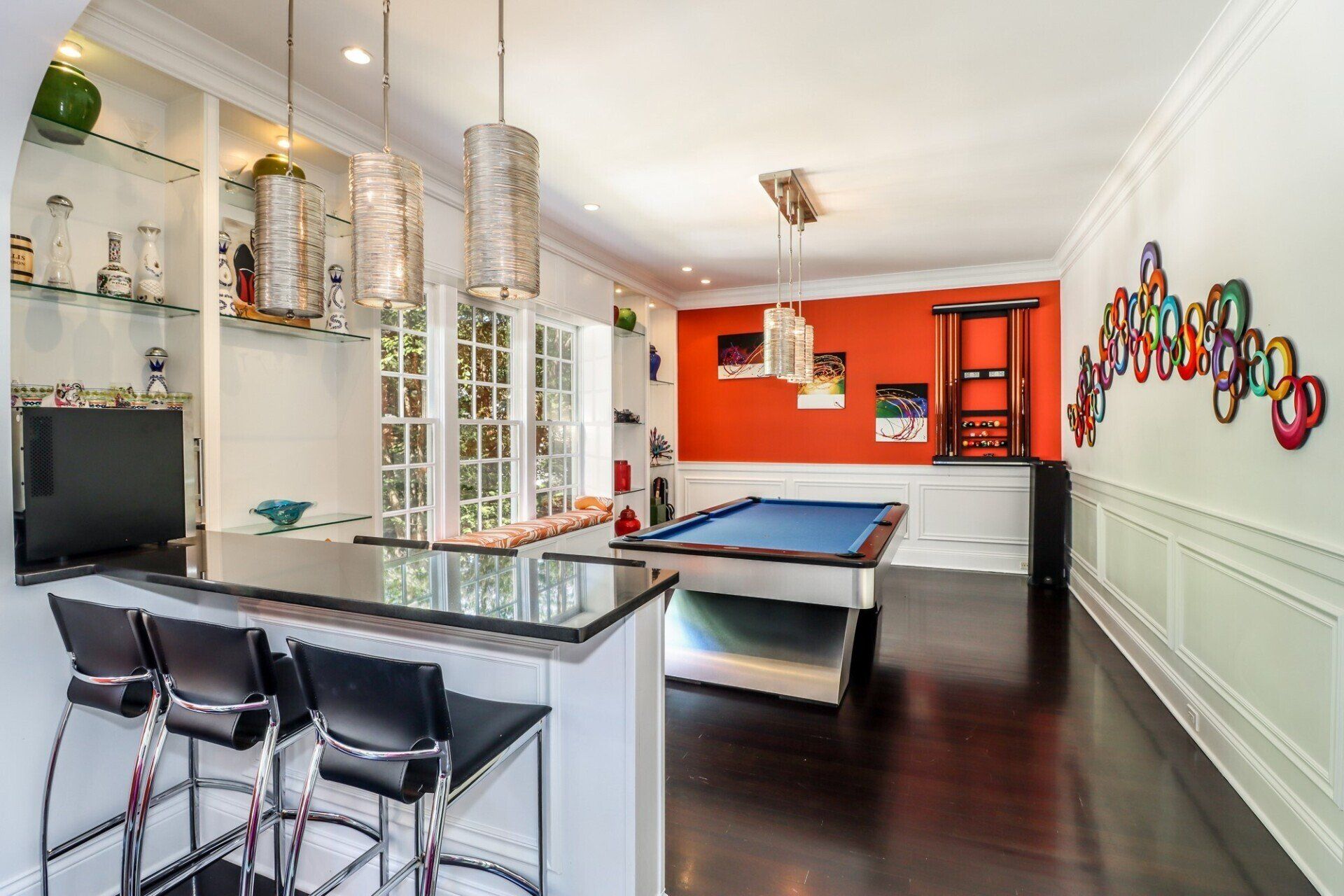 A game room with a pool table, bar, and modern lighting; an orange accent wall.