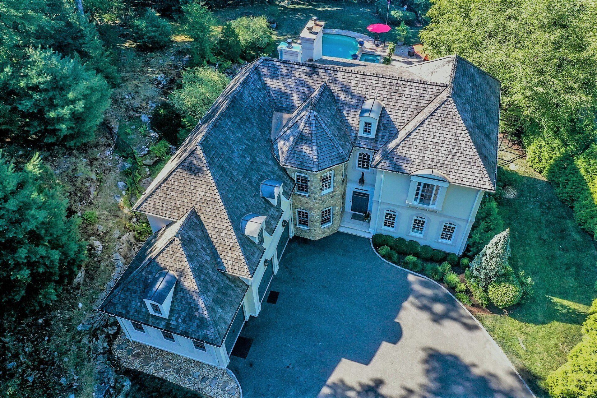Aerial view of a large house with a long driveway and a pool in the backyard, surrounded by trees.