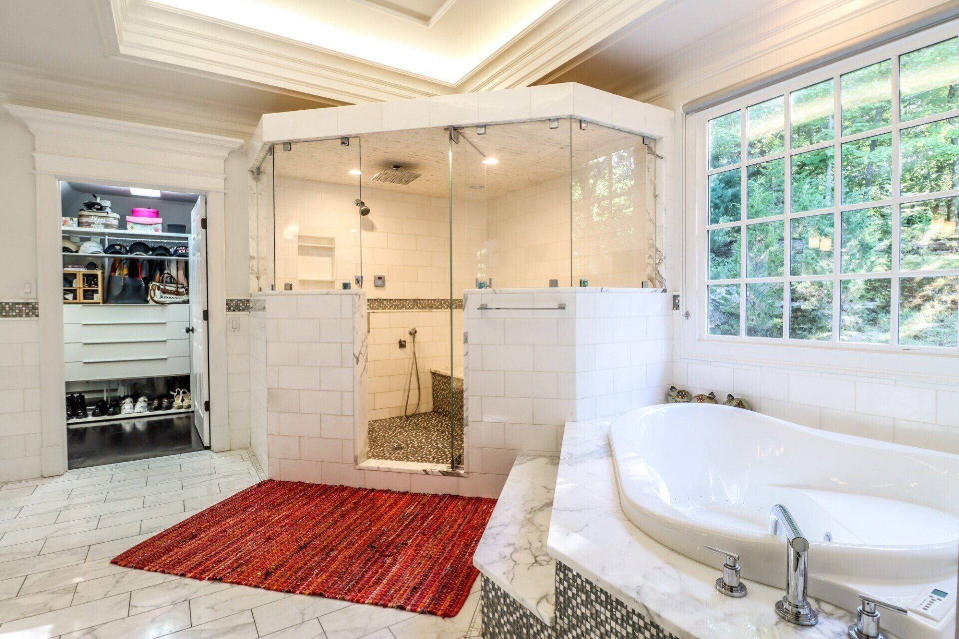 Spacious white bathroom with a walk-in shower, soaking tub, and walk-in closet. Red rug on floor.
