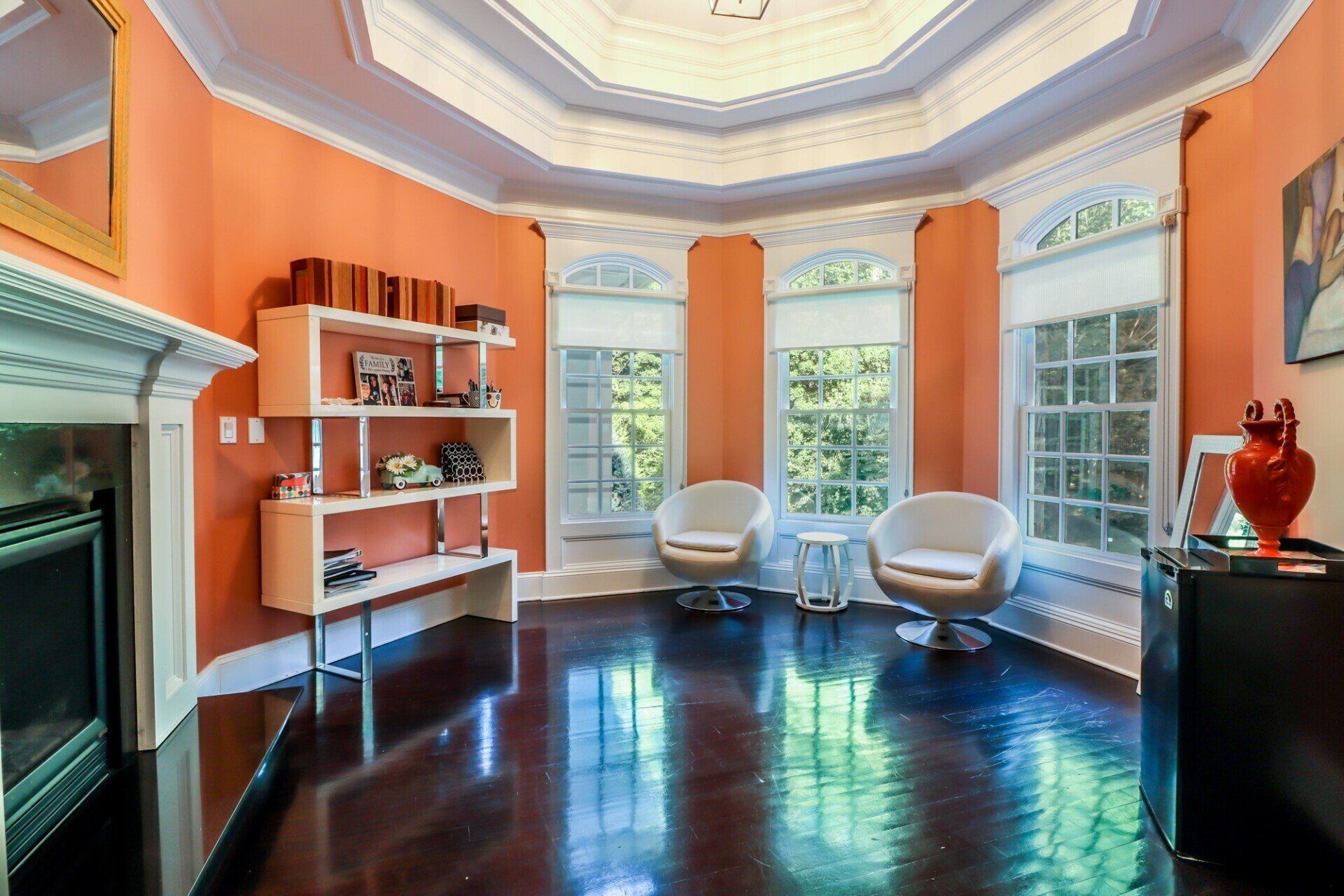 Orange room with dark wood floor, fireplace, windows, white chairs, and a unique ceiling design.