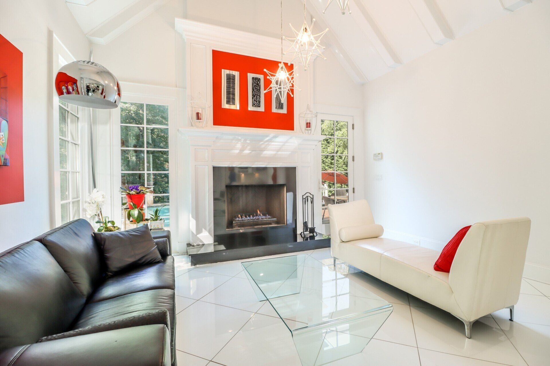 Bright living room with fireplace, white walls, black leather couch, white chaise, and red art.