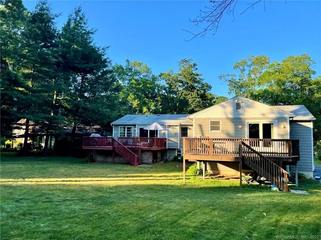 Two houses with wooden decks, surrounded by green lawn and trees.