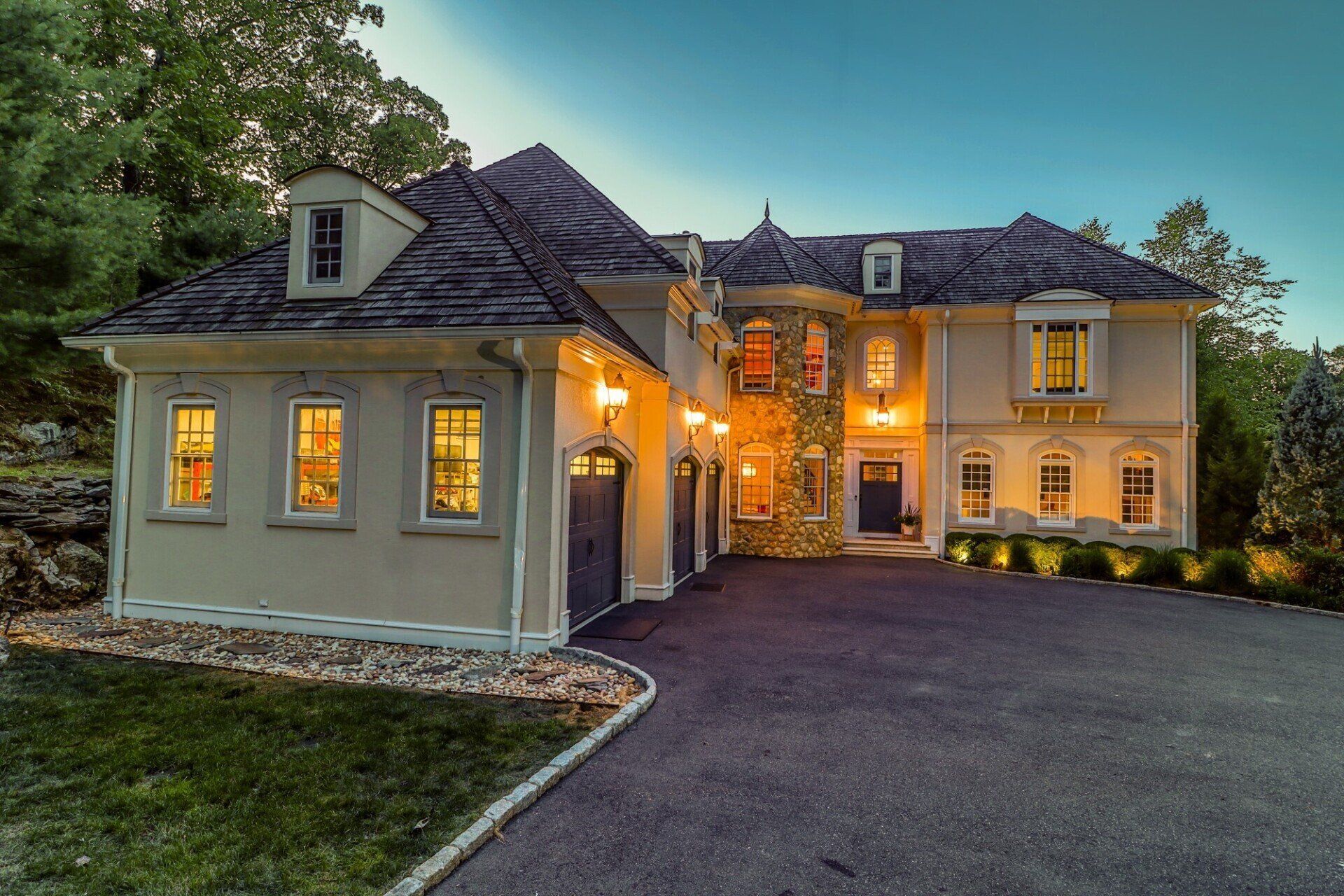Luxurious home with a stone facade, lit windows, and a dark driveway.