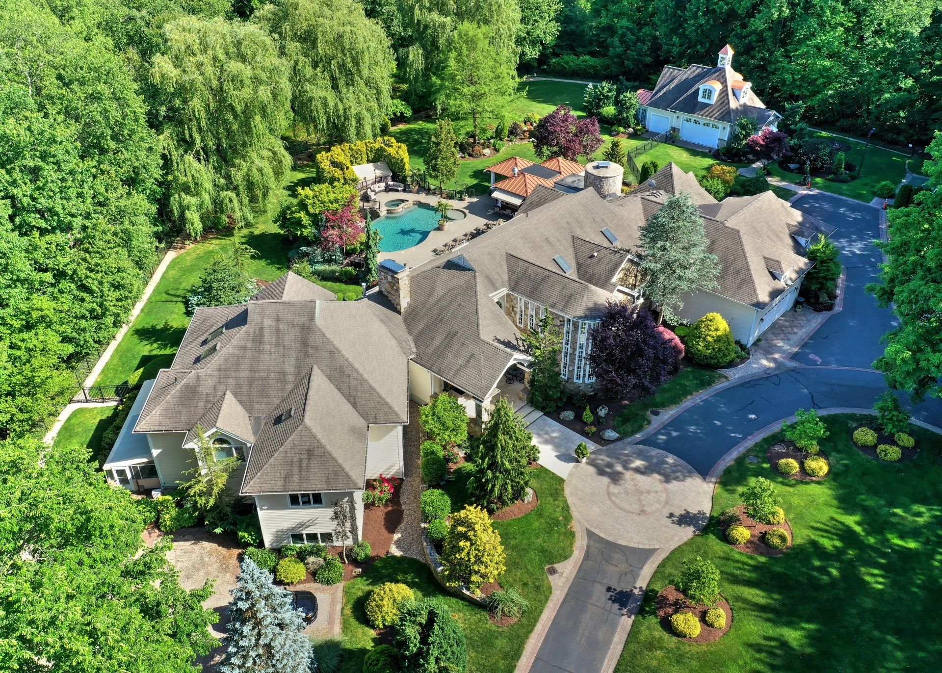 Aerial view of a large estate with a house, pool, landscaping, and a circular driveway.