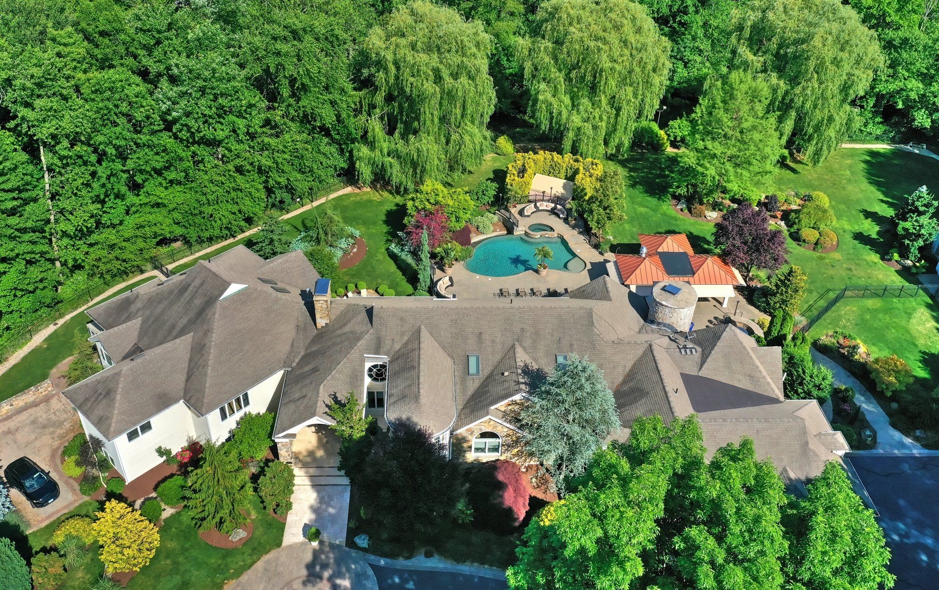 Aerial view of a large house with a pool and lush greenery; trees surround the property.