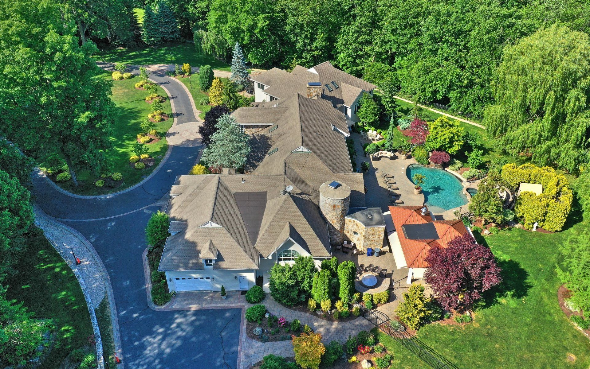 Aerial view of a large house with a pool and lush greenery. A winding driveway leads to the property.