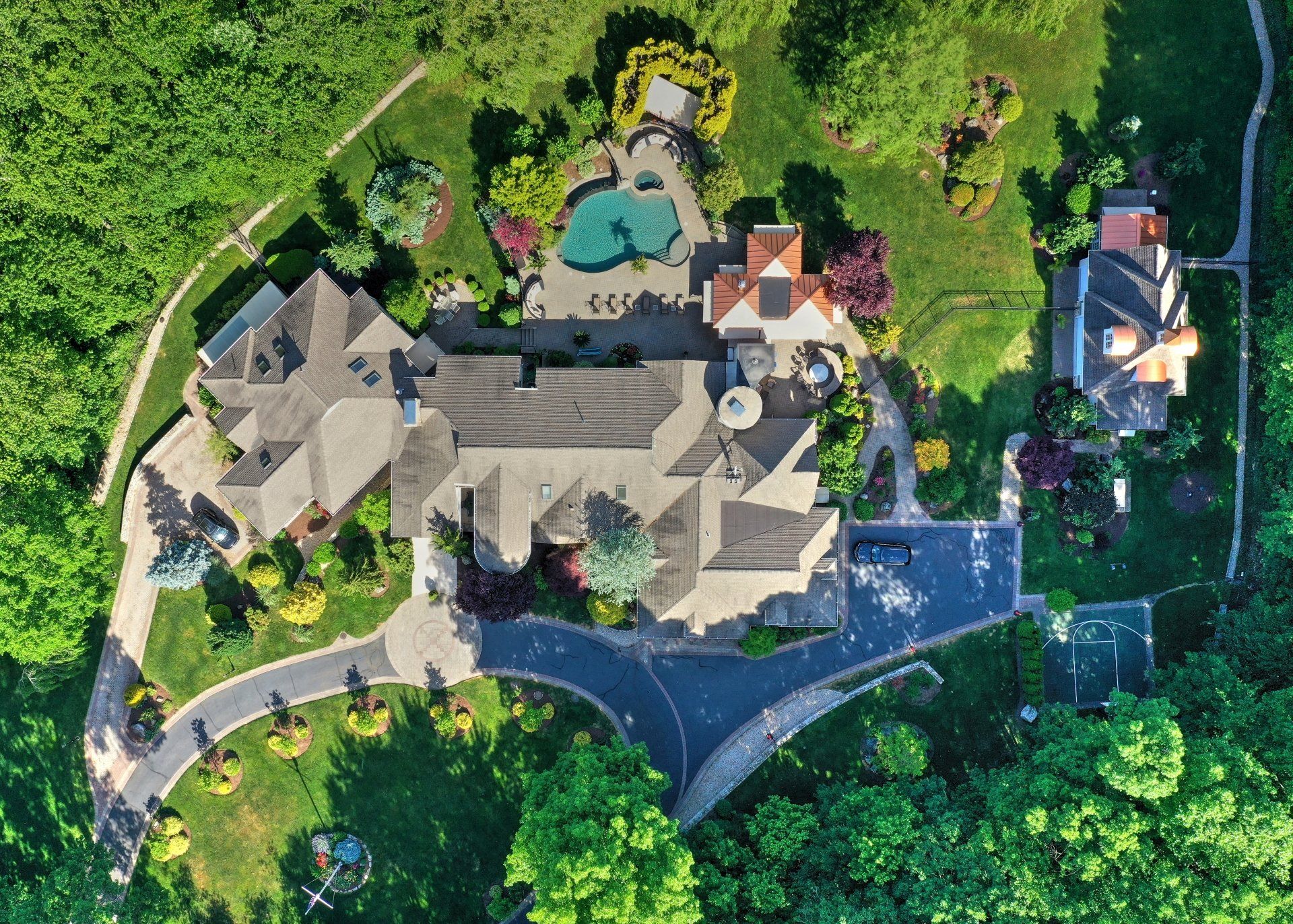 Aerial view of a large estate with a pool, lush landscaping, and long driveway.
