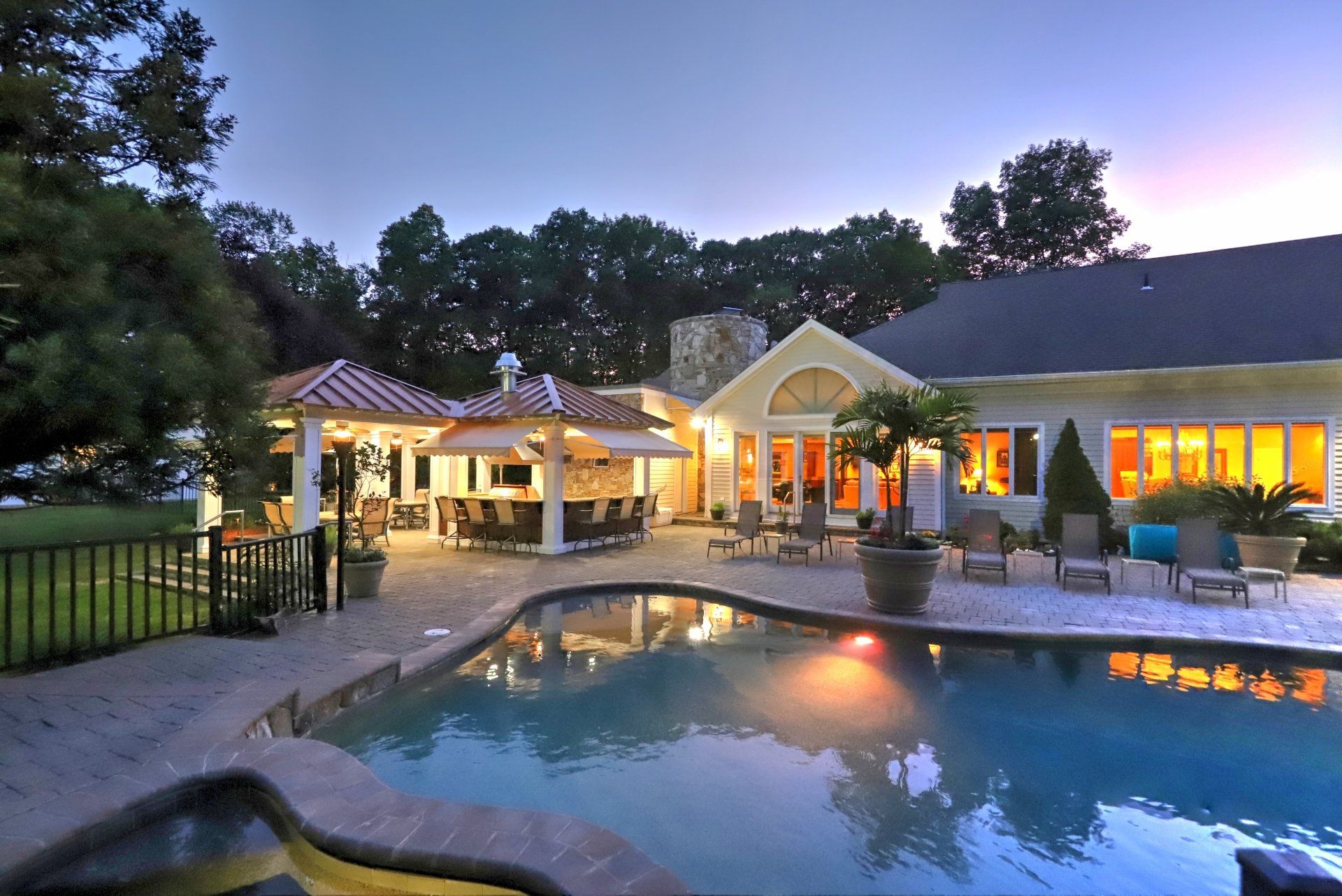 Backyard scene with pool, outdoor bar, and illuminated house at dusk.