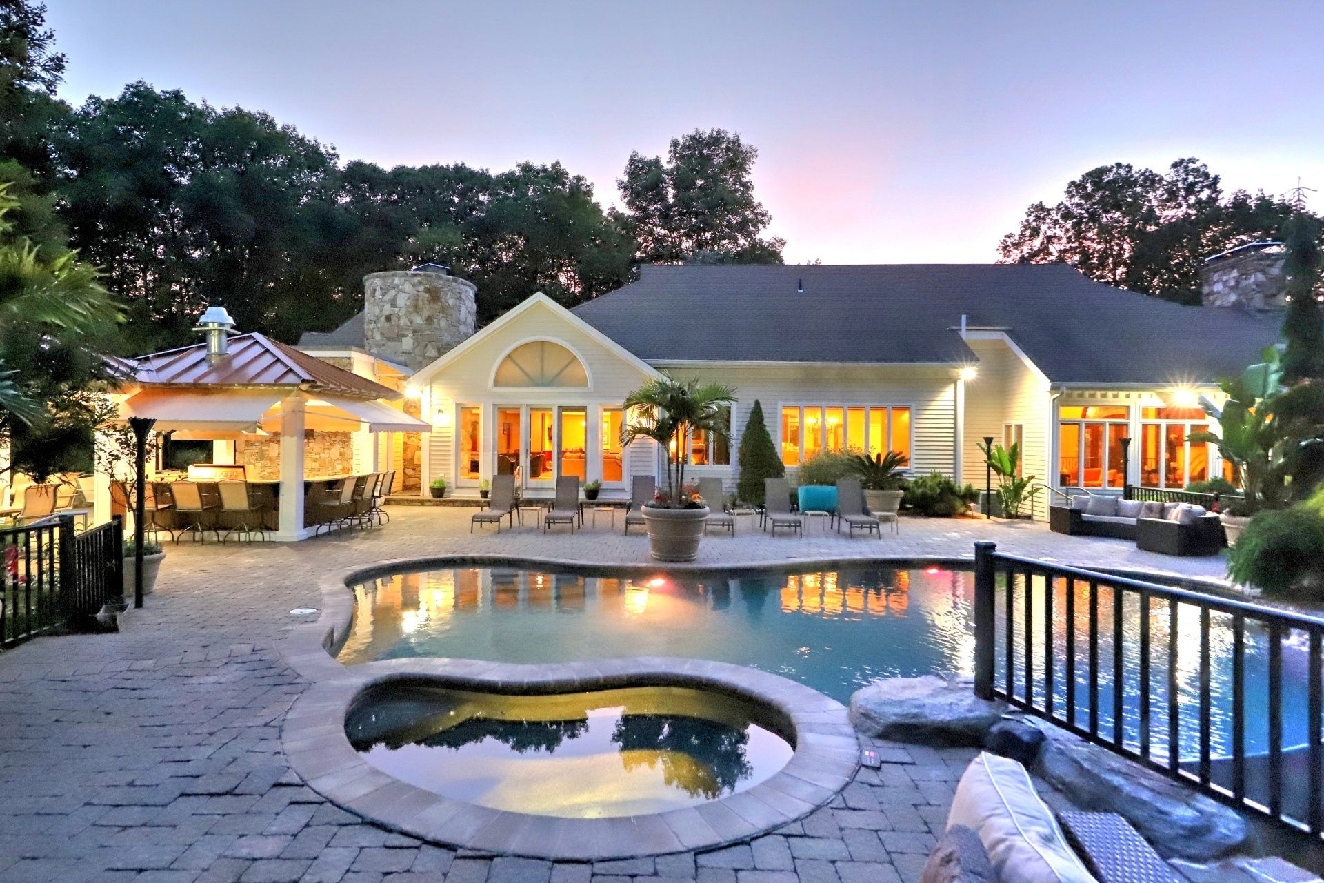 Luxury home exterior with pool and gazebo at dusk.