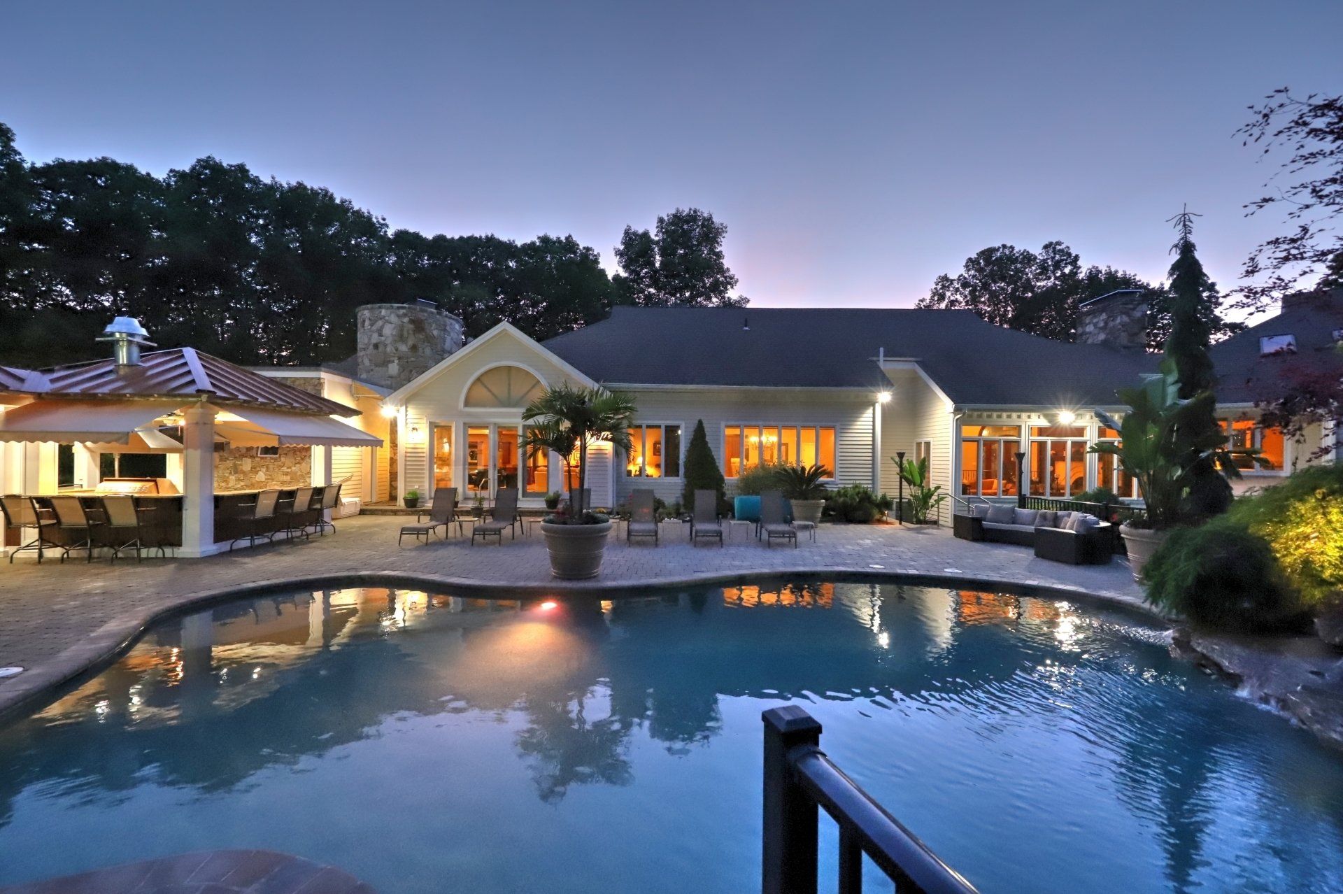 Pool and outdoor bar area at dusk, luxury home with lights reflecting in the water.