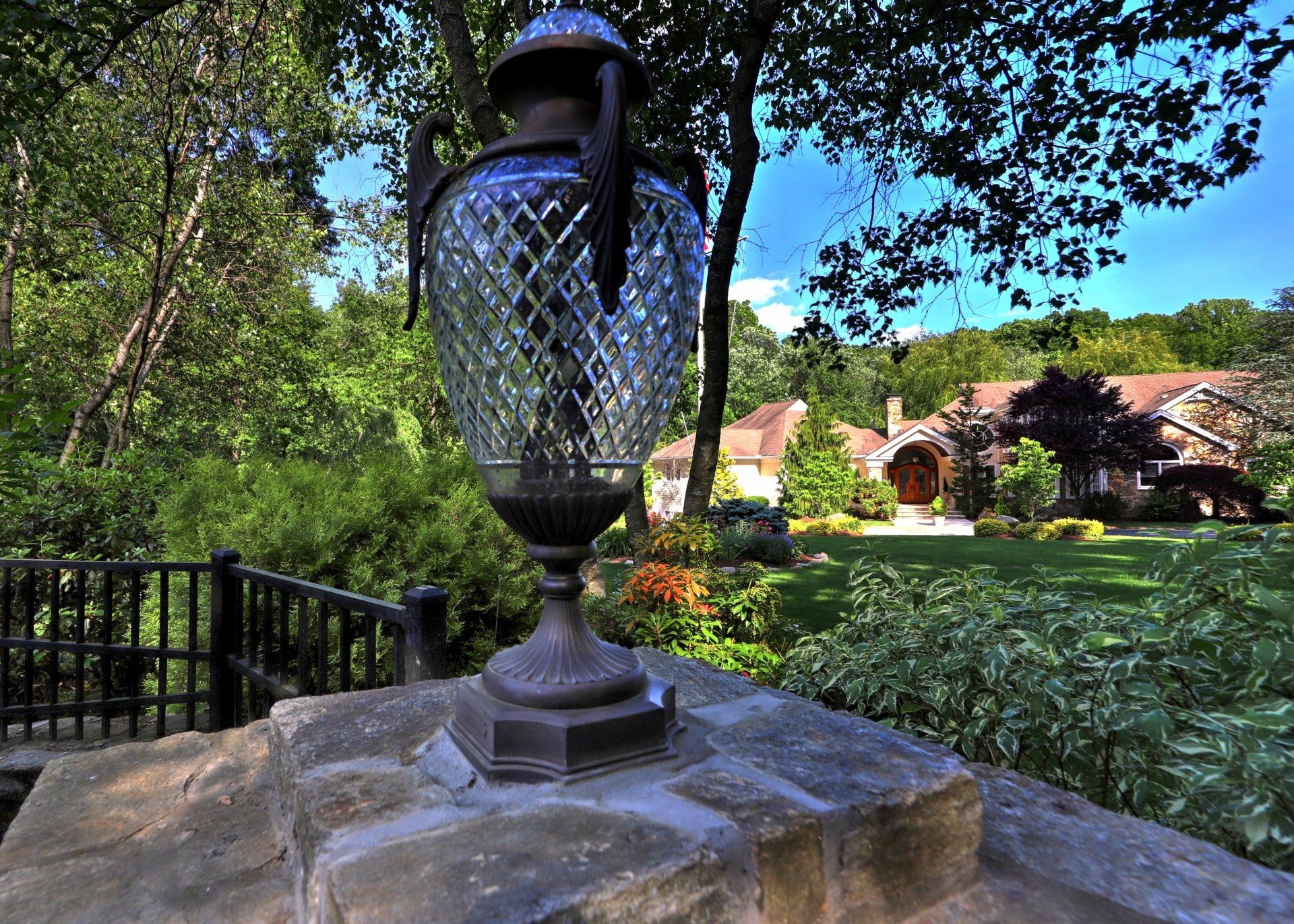 Ornate lamp on stone wall overlooking a large house with lush landscaping.