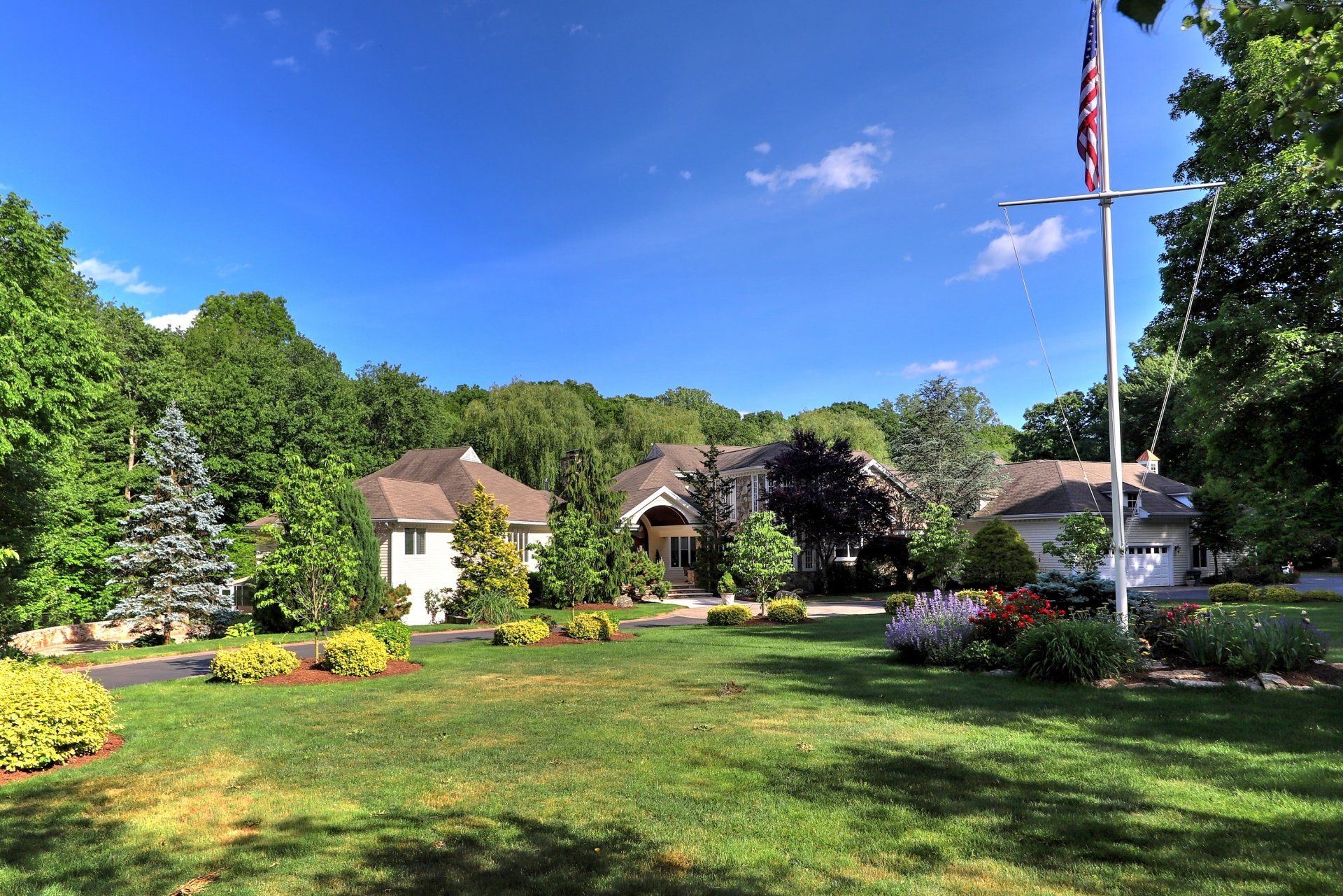 Large suburban home with American flag on a sunny day. Green lawn and trees surround the house.