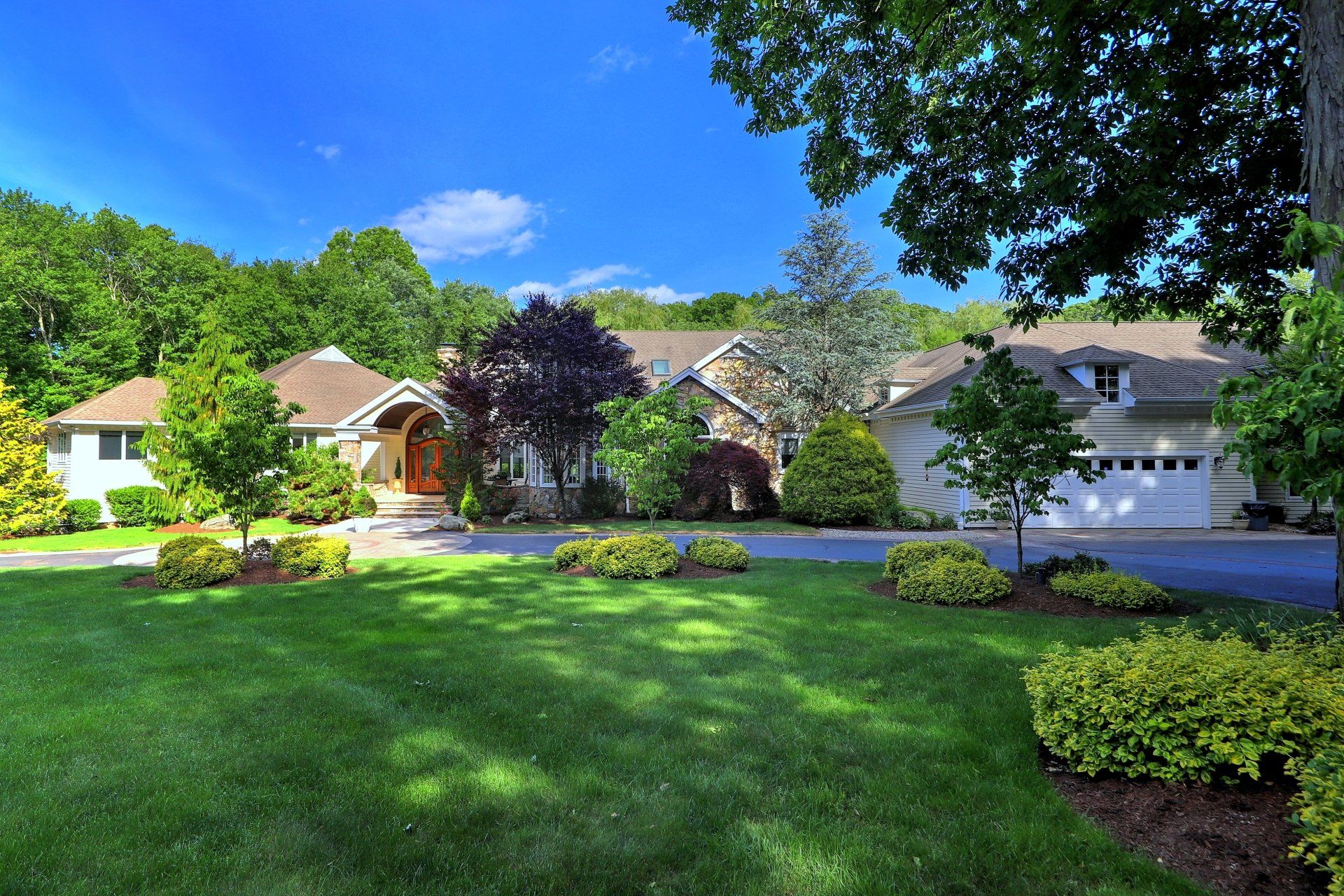 Large house with a well-manicured lawn, trees, and blue sky.