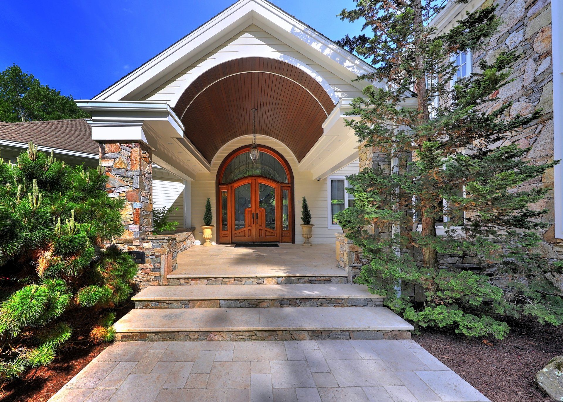 Elegant home entrance with arched portico, stone accents, double wooden doors, and steps.