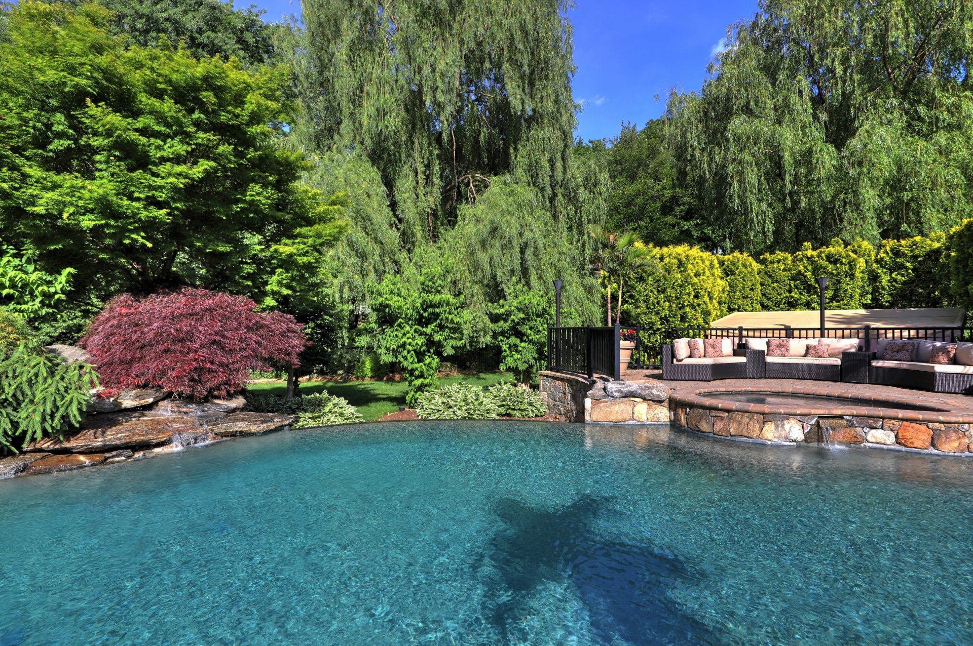 Pool with turquoise water surrounded by lush greenery and lounge area under a bright blue sky.
