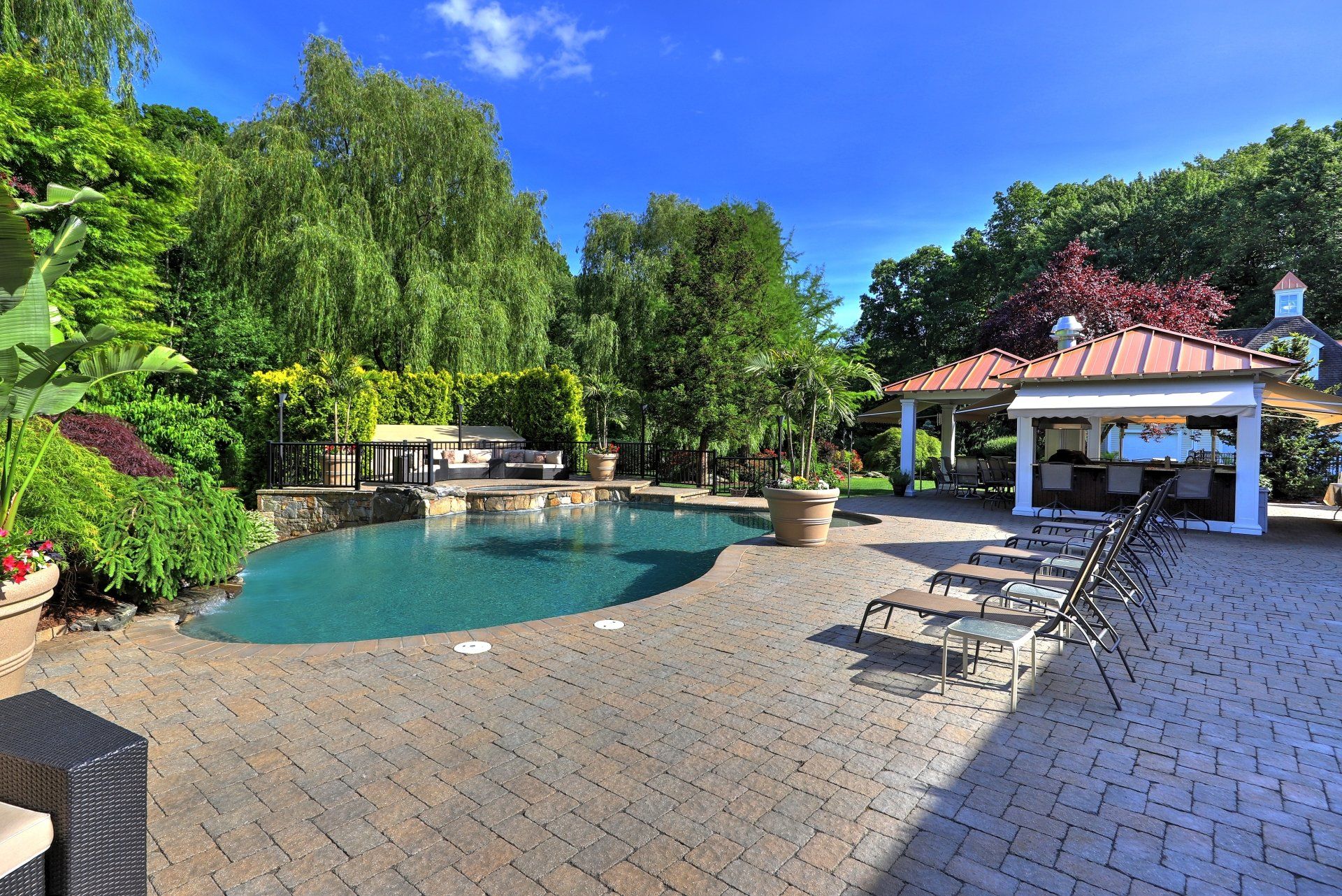 Backyard pool with patio, lounge chairs, and a covered bar, under a sunny blue sky.