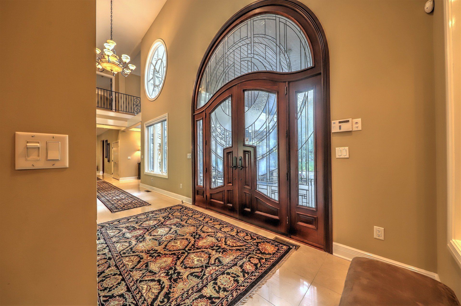 Grand entrance with ornate wooden door, stained glass, and area rugs on a light-colored floor.