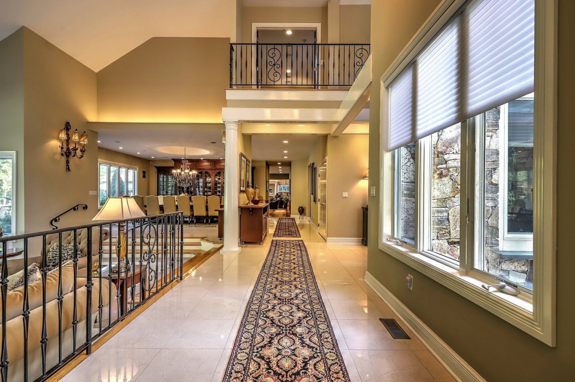 Grand foyer with ornate railing, patterned rug, and large windows.