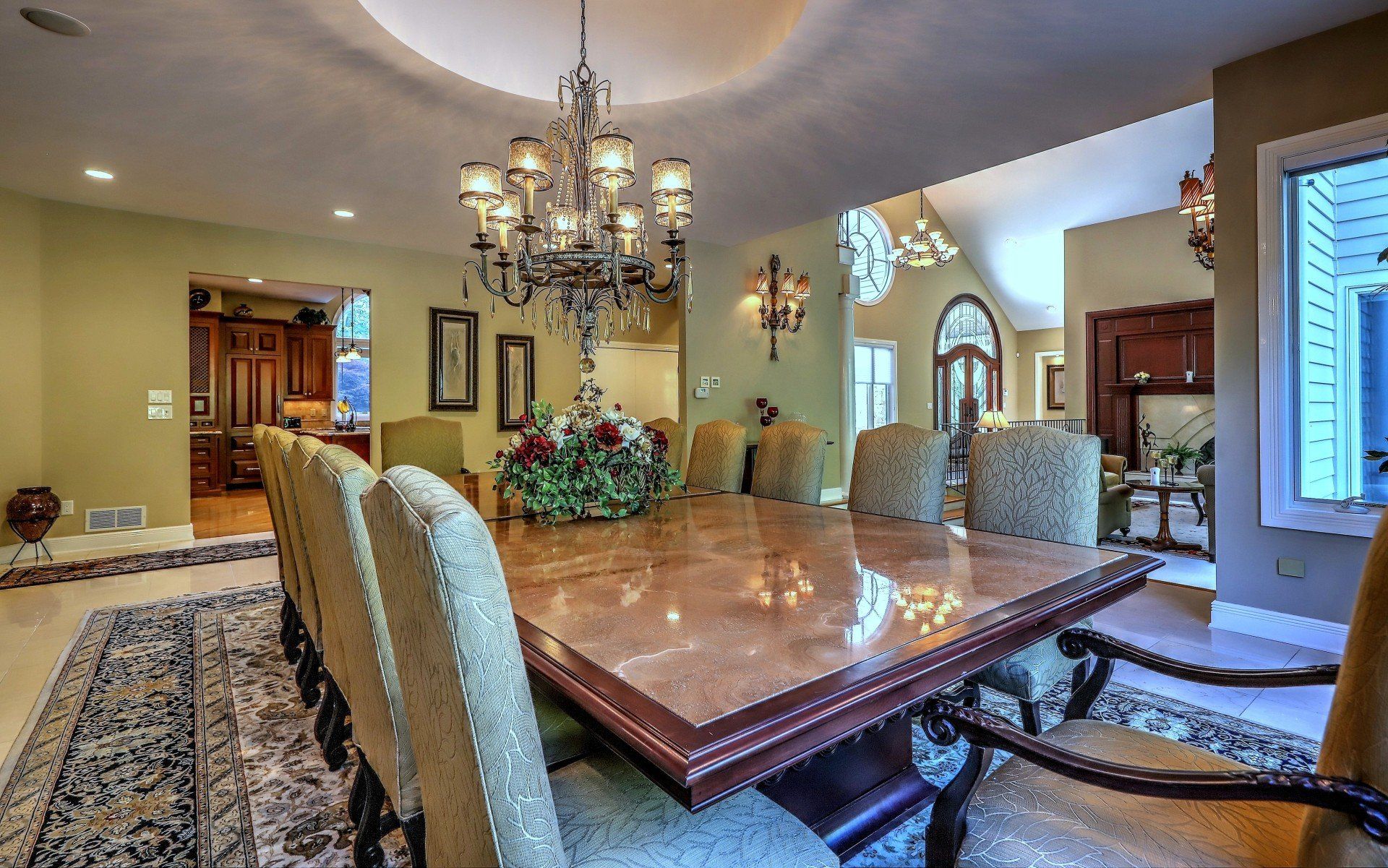 Elegant dining room with large table, chandelier, and upholstered chairs.