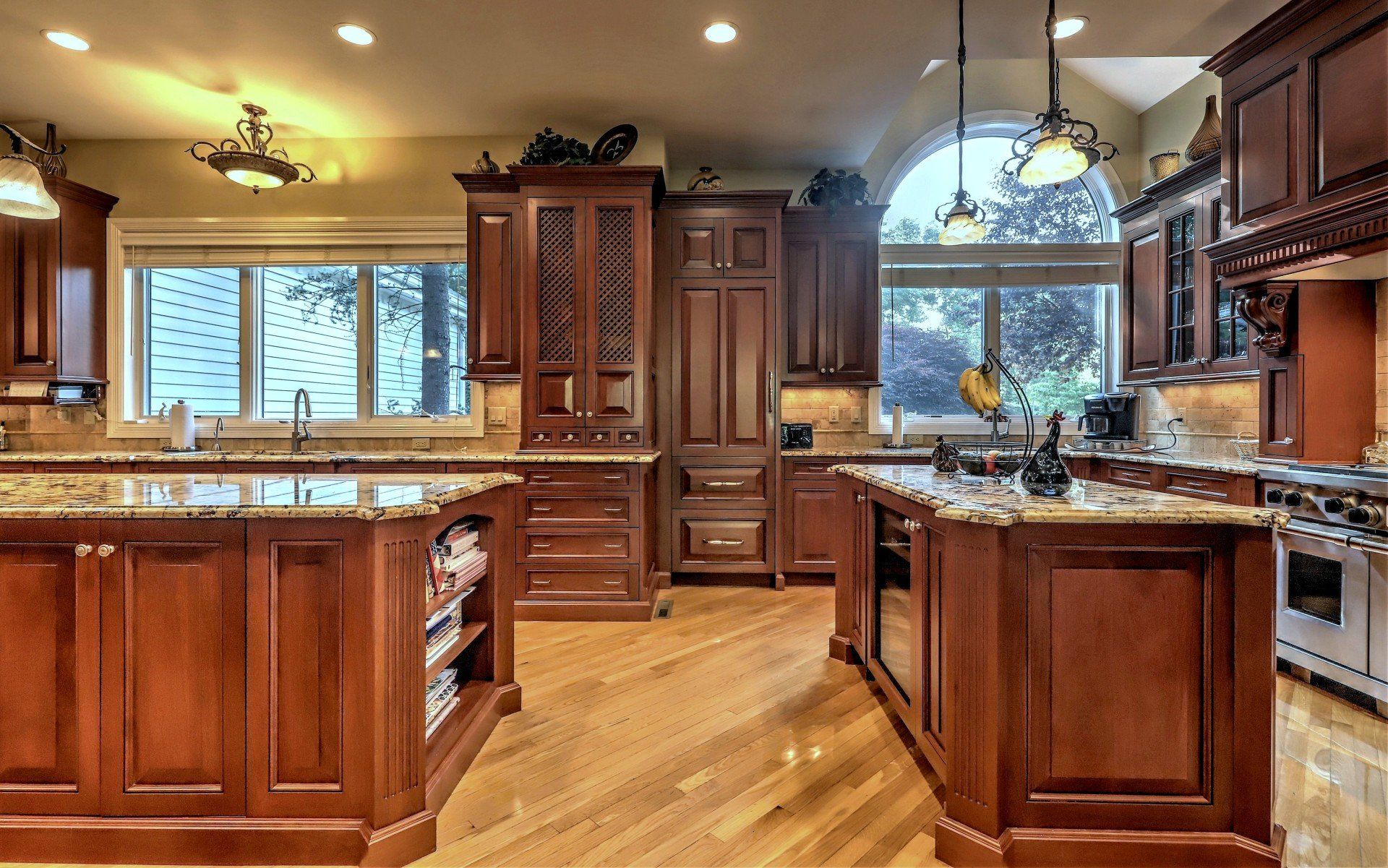 Spacious kitchen with wood cabinets, granite countertops, and two islands, featuring windows, appliances, overhead lights.