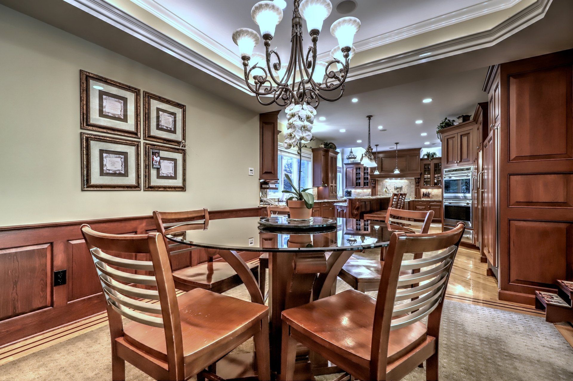 Dining room with glass table, four chairs, chandelier, and a view of the kitchen.