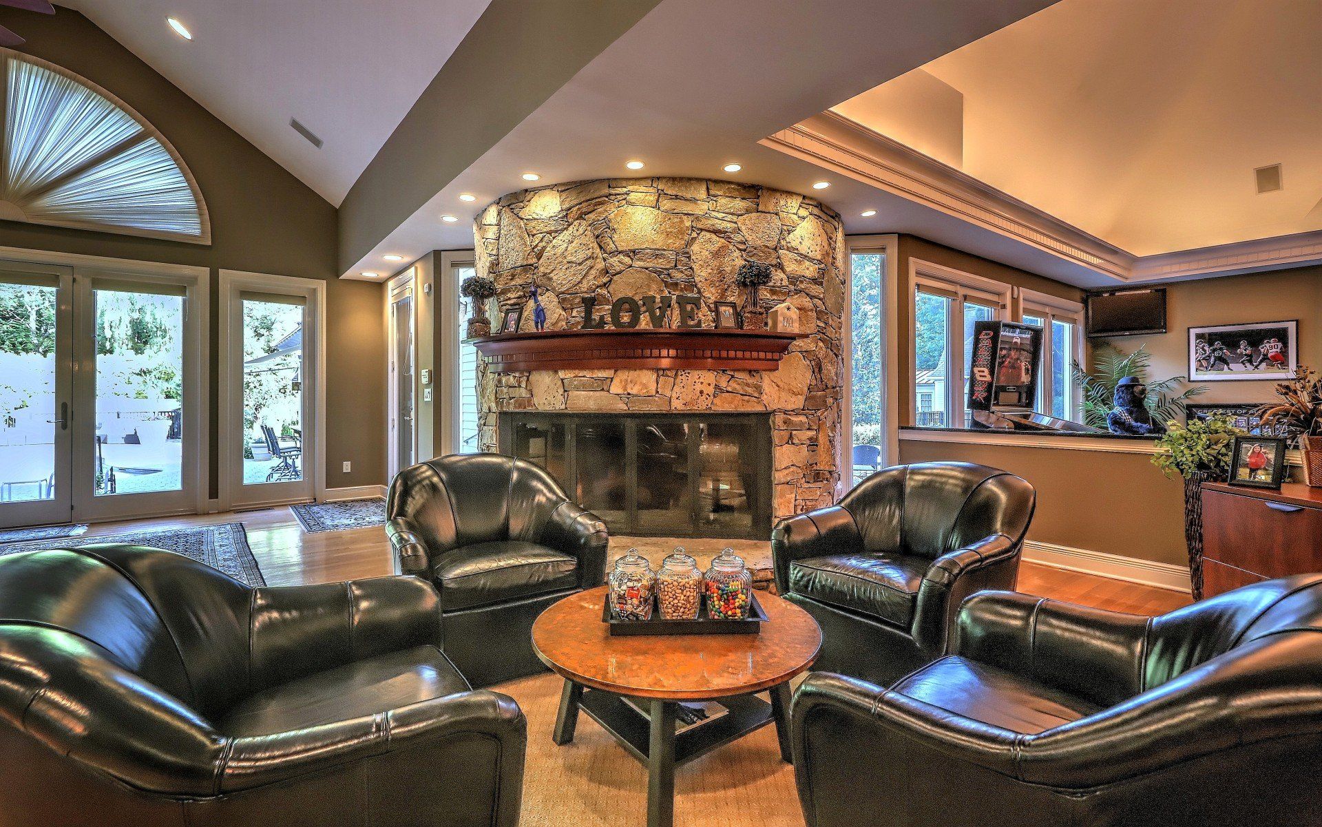 Living room with a stone fireplace, four black leather chairs, and a round wooden table.
