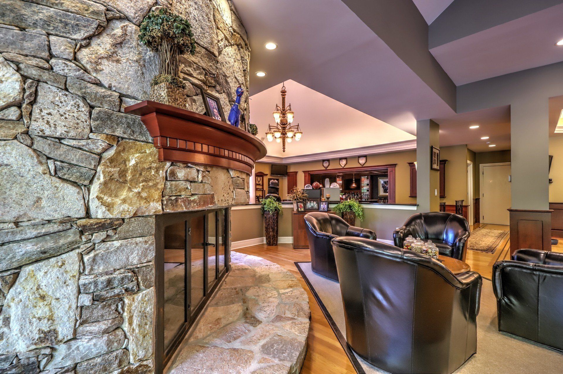Stone fireplace with wooden mantel in a room with black leather chairs and a chandelier.